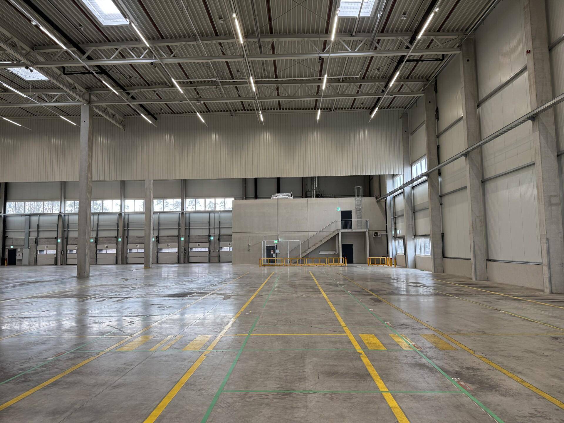 Geräumige Lagerhalle mit hohen Decken, Betonboden und mehreren Rolltoren für den Warenumschlag.