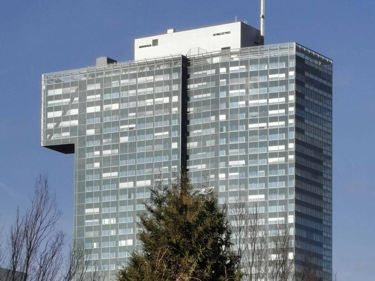 Nahaufnahme eines modernen Hochhauses mit vielen Fenstern und einer markanten architektonischen Auskragung.