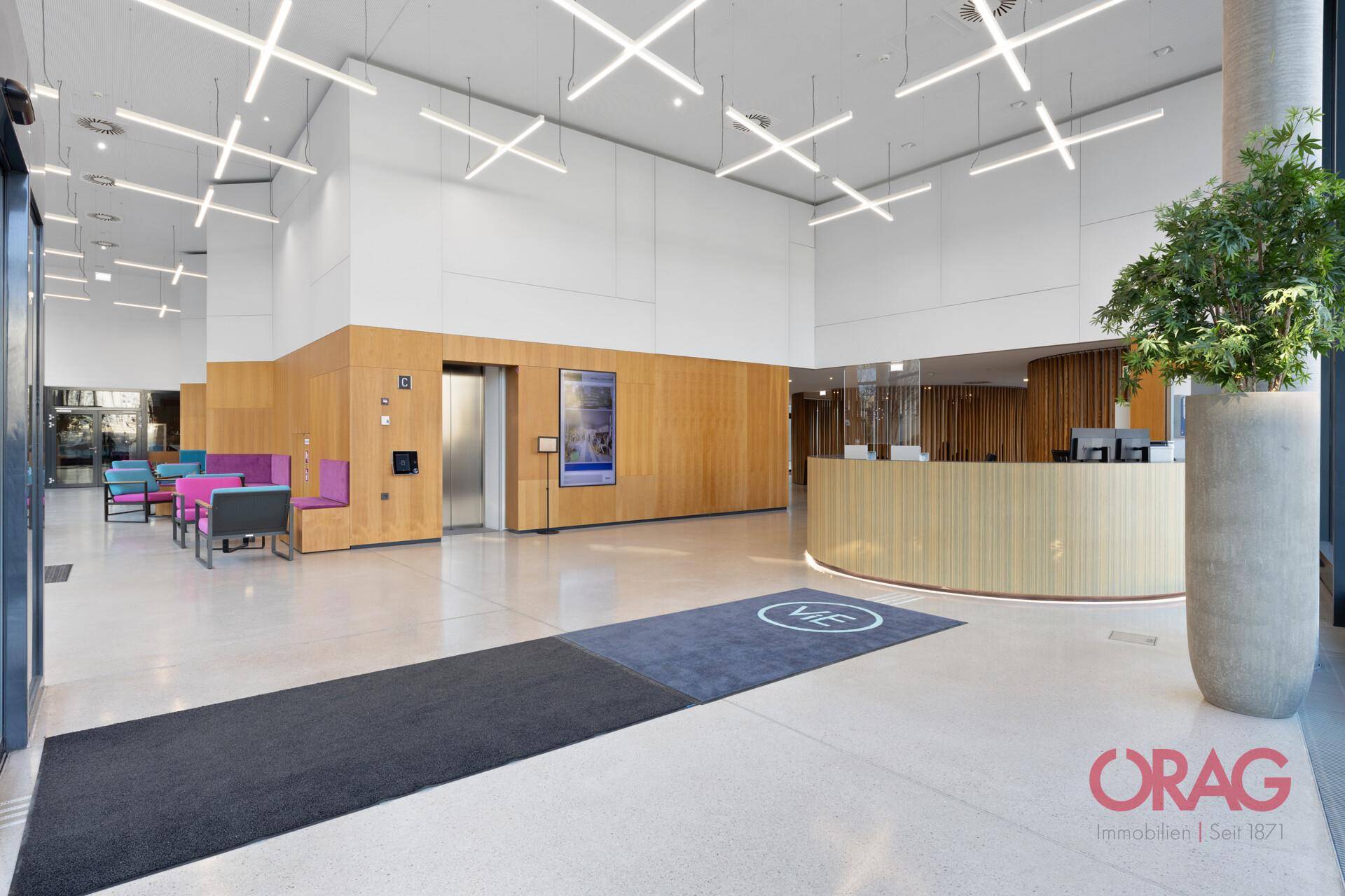 Geräumige, moderne Lobby mit Rezeption, Aufzug und stilvollen Sitzgelegenheiten in hellem Design.