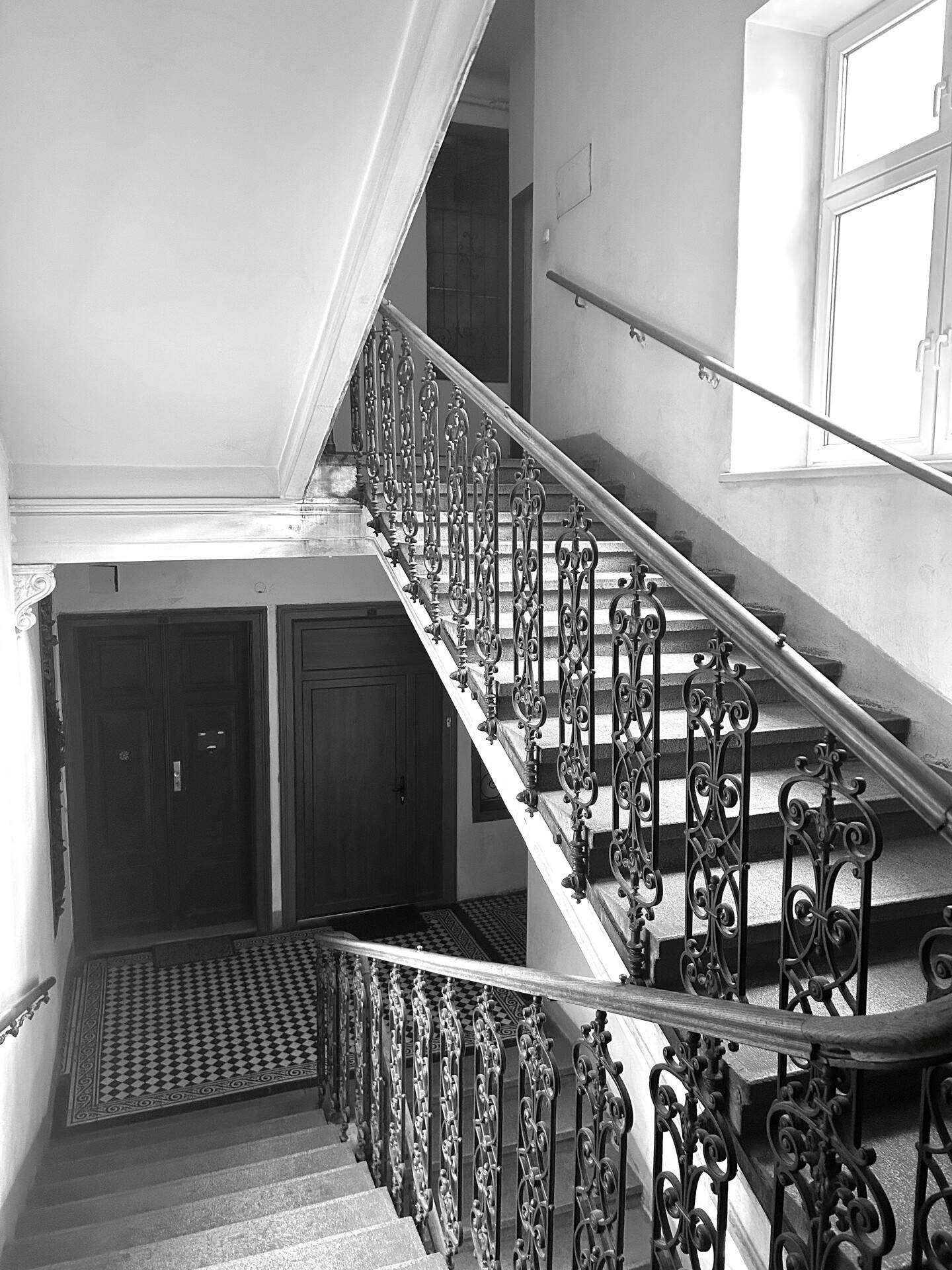 Historisches Treppenhaus mit schmiedeeisernem Geländer, hohen Decken und natürlichem Lichteinfall.