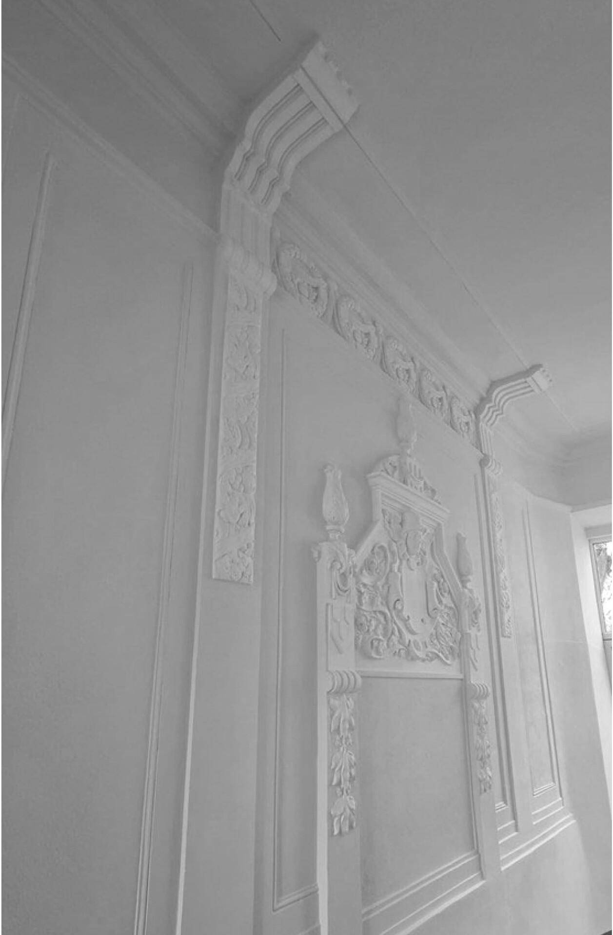 Wand mit aufwendigen Stuckverzierungen und einem Fenster, das natürliches Licht hereinlässt.