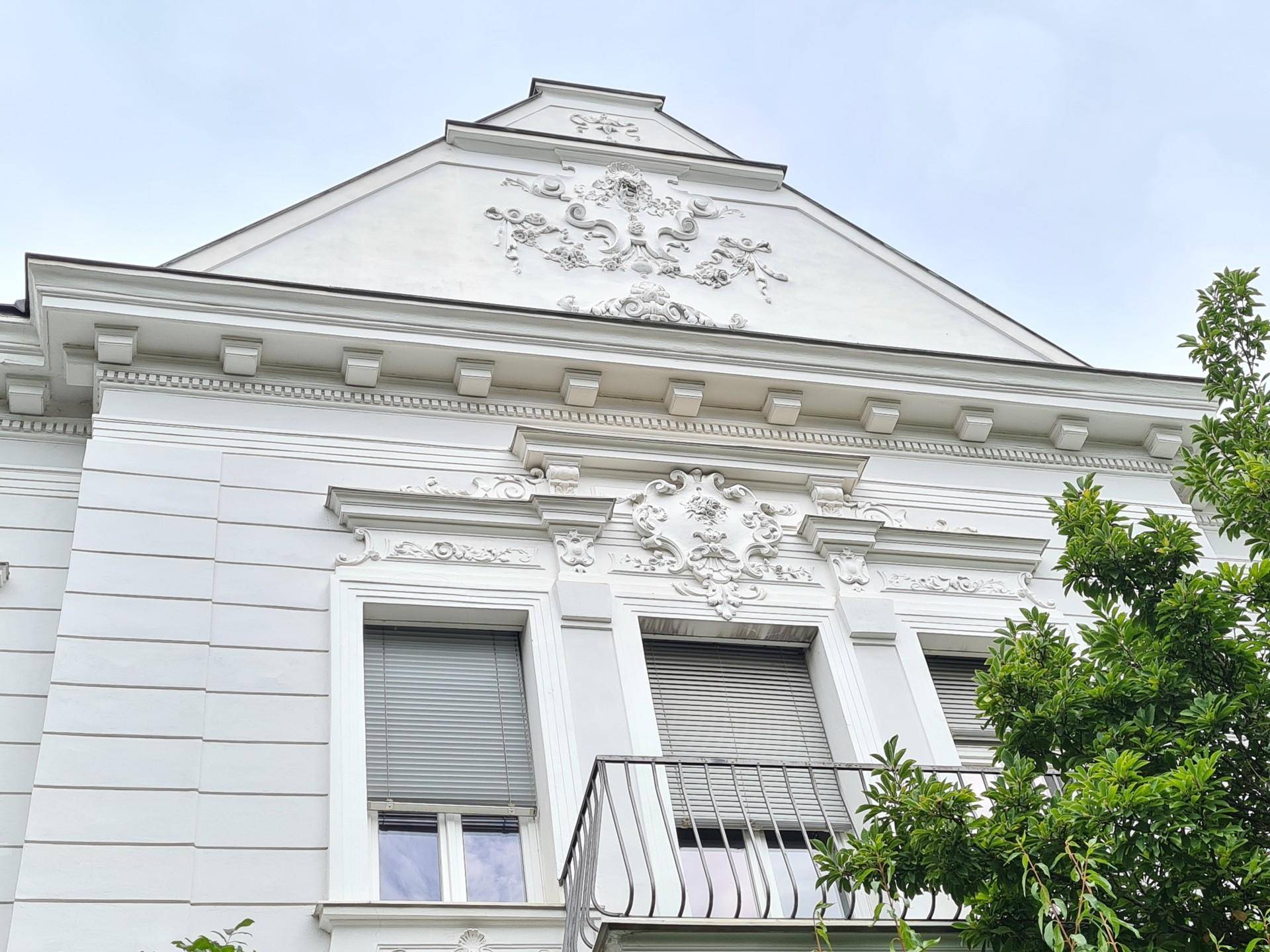 Detailansicht der historischen Fassade mit aufwendigem Stuckdekor, Fenstern und einem kleinen Balkon.