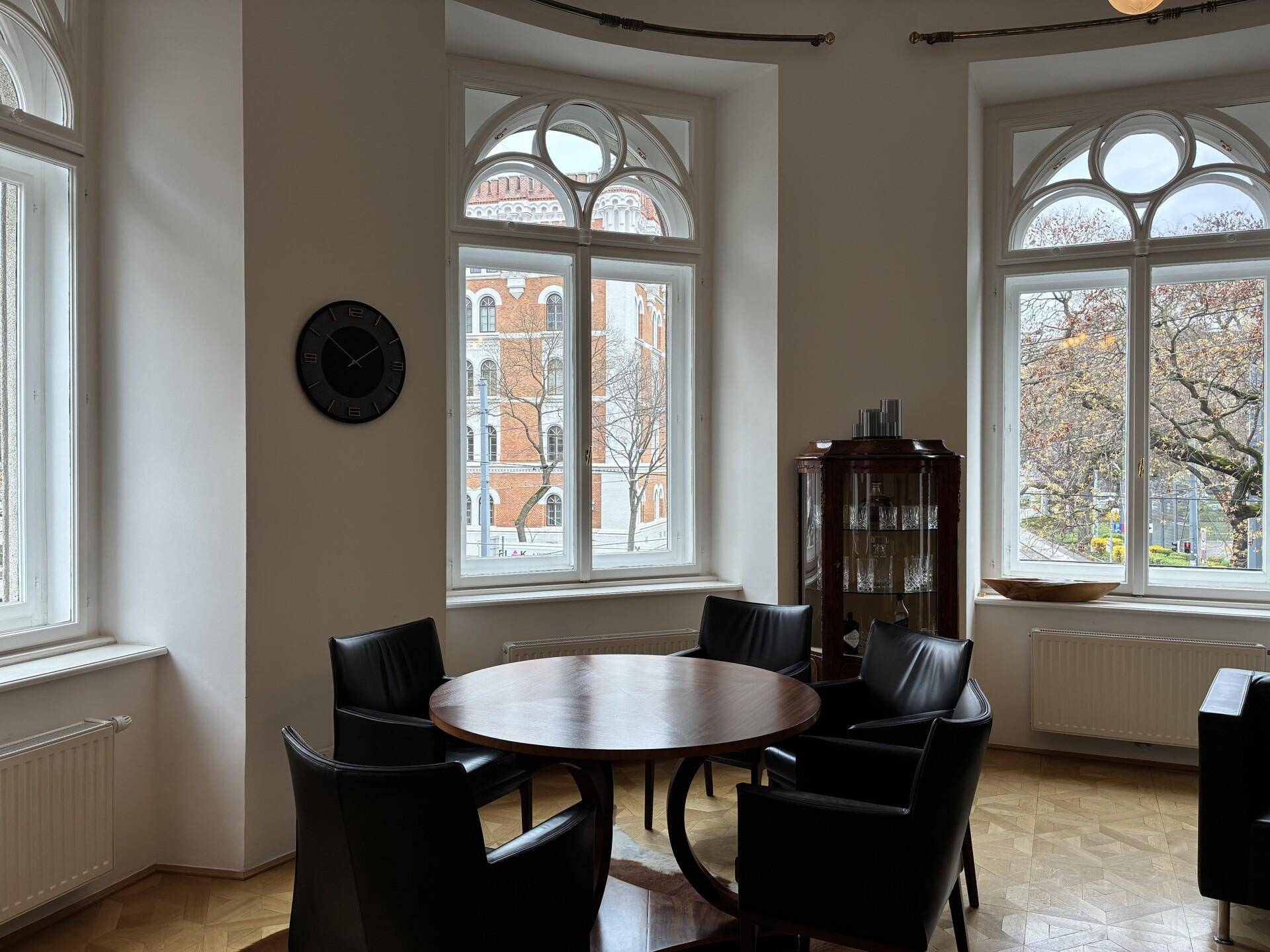 Gemütlicher Loungebereich mit runden Tischen, bequemen Ledersesseln und dekorativen Bogenfenstern.