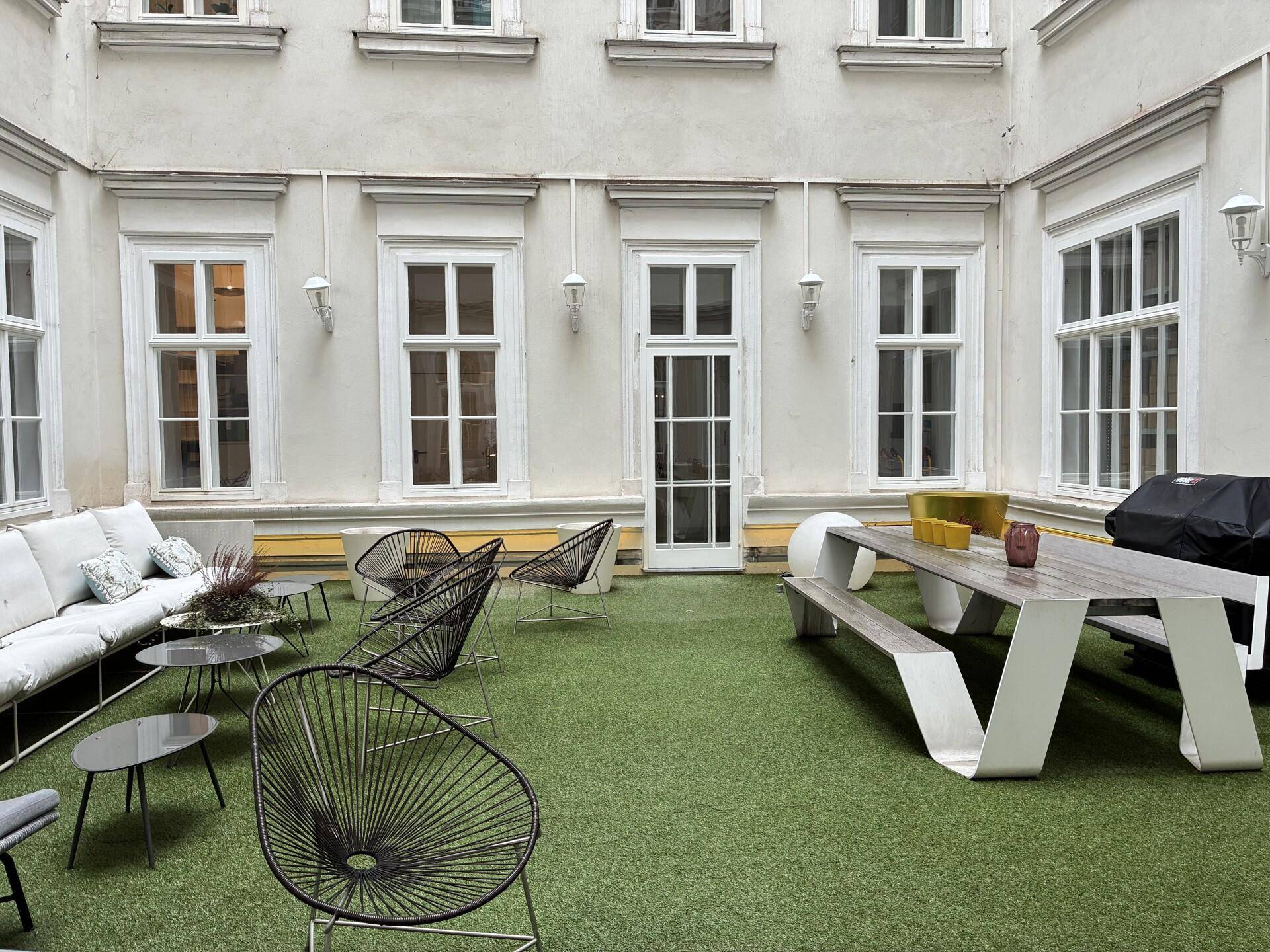 Moderner Innenhof mit Kunstrasen, stilvollen Gartenmöbeln und einem großen Esstisch im Freien.