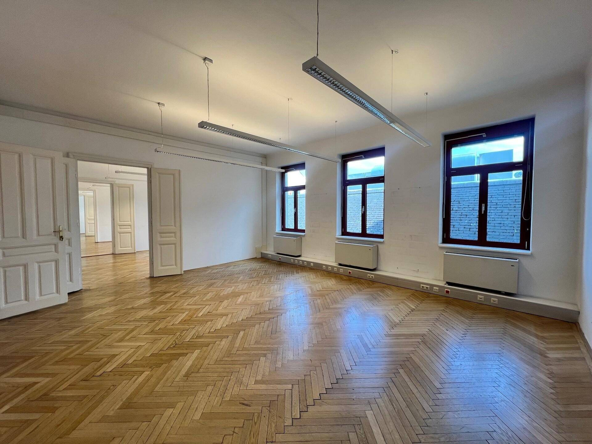 Helles Büro mit Fischgrätparkett und Blick in angrenzende Räume durch offene Türen.