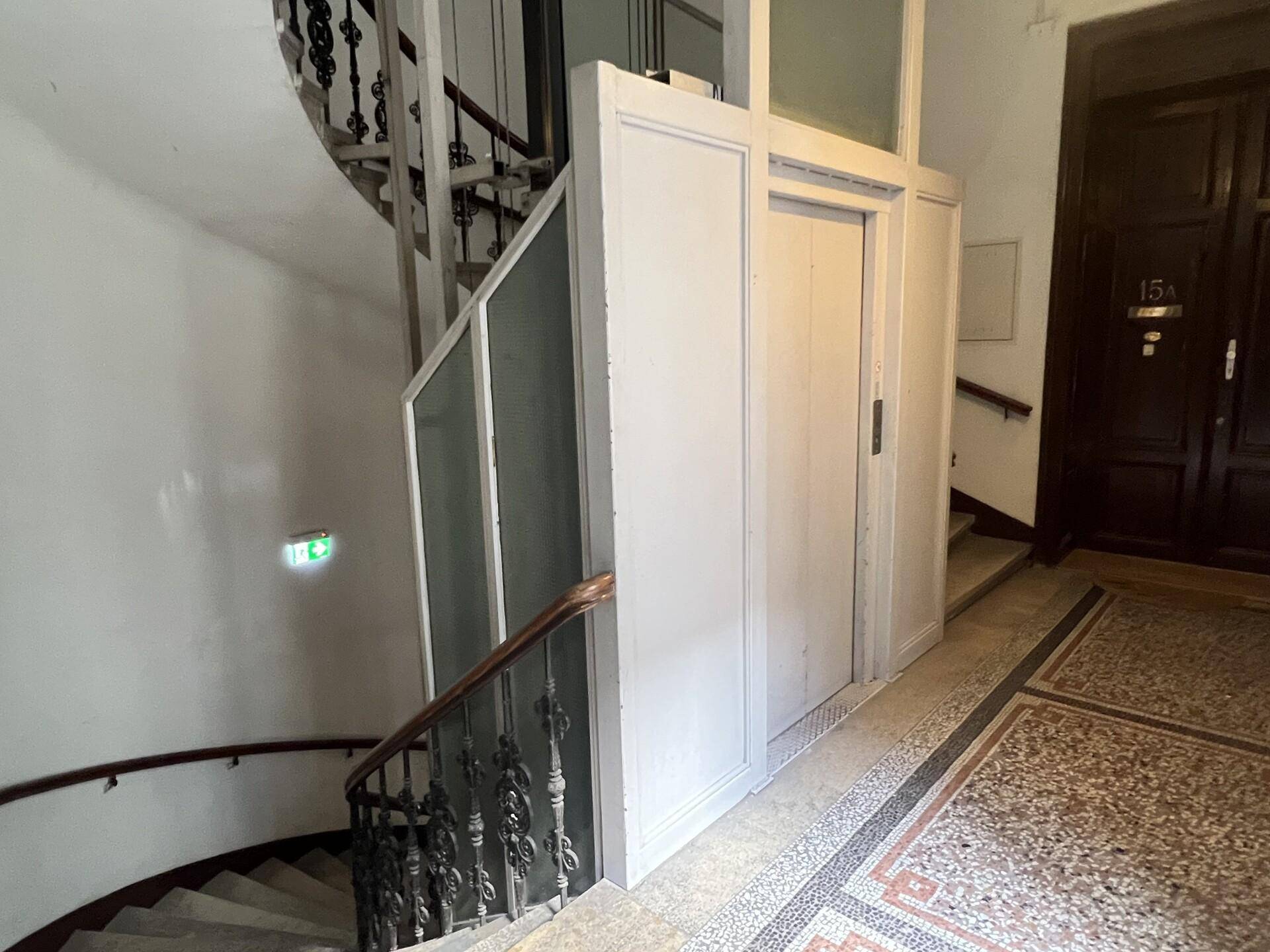 Historisches Treppenhaus mit schmiedeeisernem Geländer und einem klassischen Aufzug in einem Altbau.