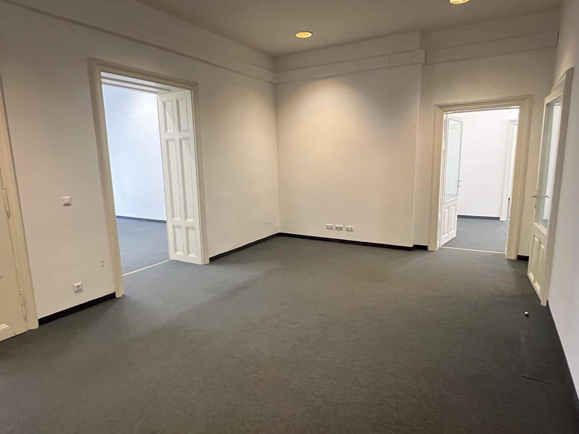 Heller Büroraum mit Teppichboden und mehreren Türen, die zu weiteren Räumen führen.