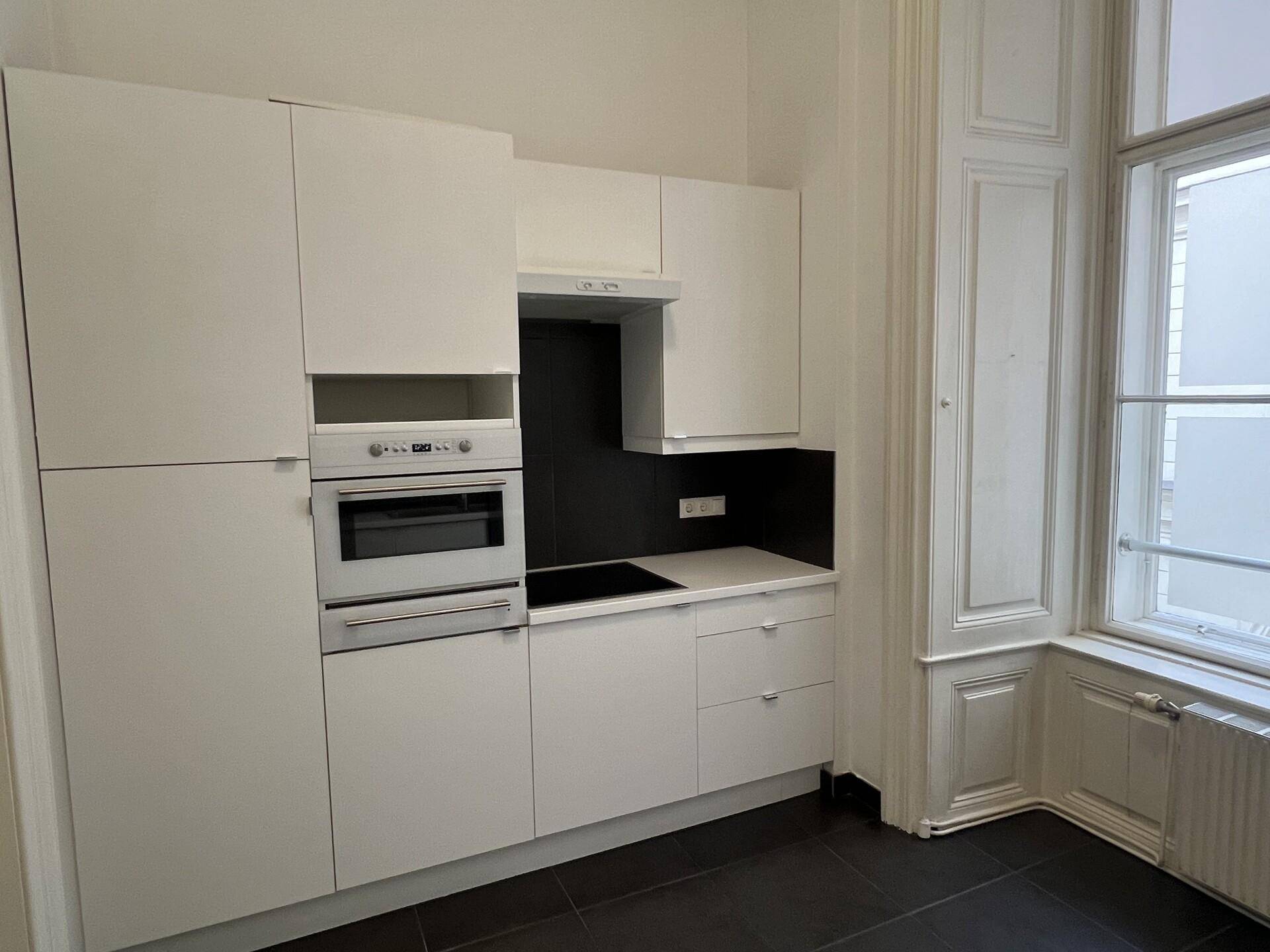 Moderne Einbauküche mit weißen Schränken, integriertem Backofen und dunklem Fliesenboden.