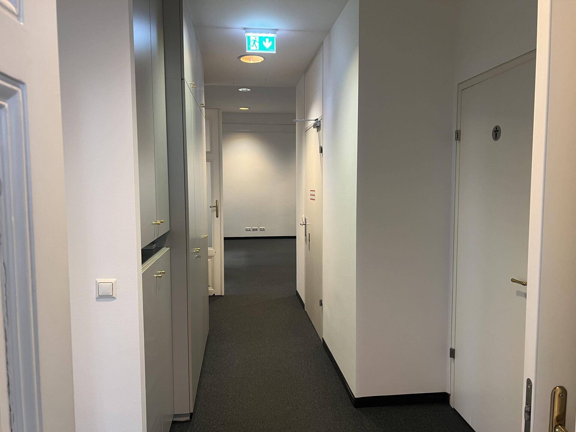 Schmaler Flur mit Einbauschränken, Teppichboden und Türen zu verschiedenen Räumen.