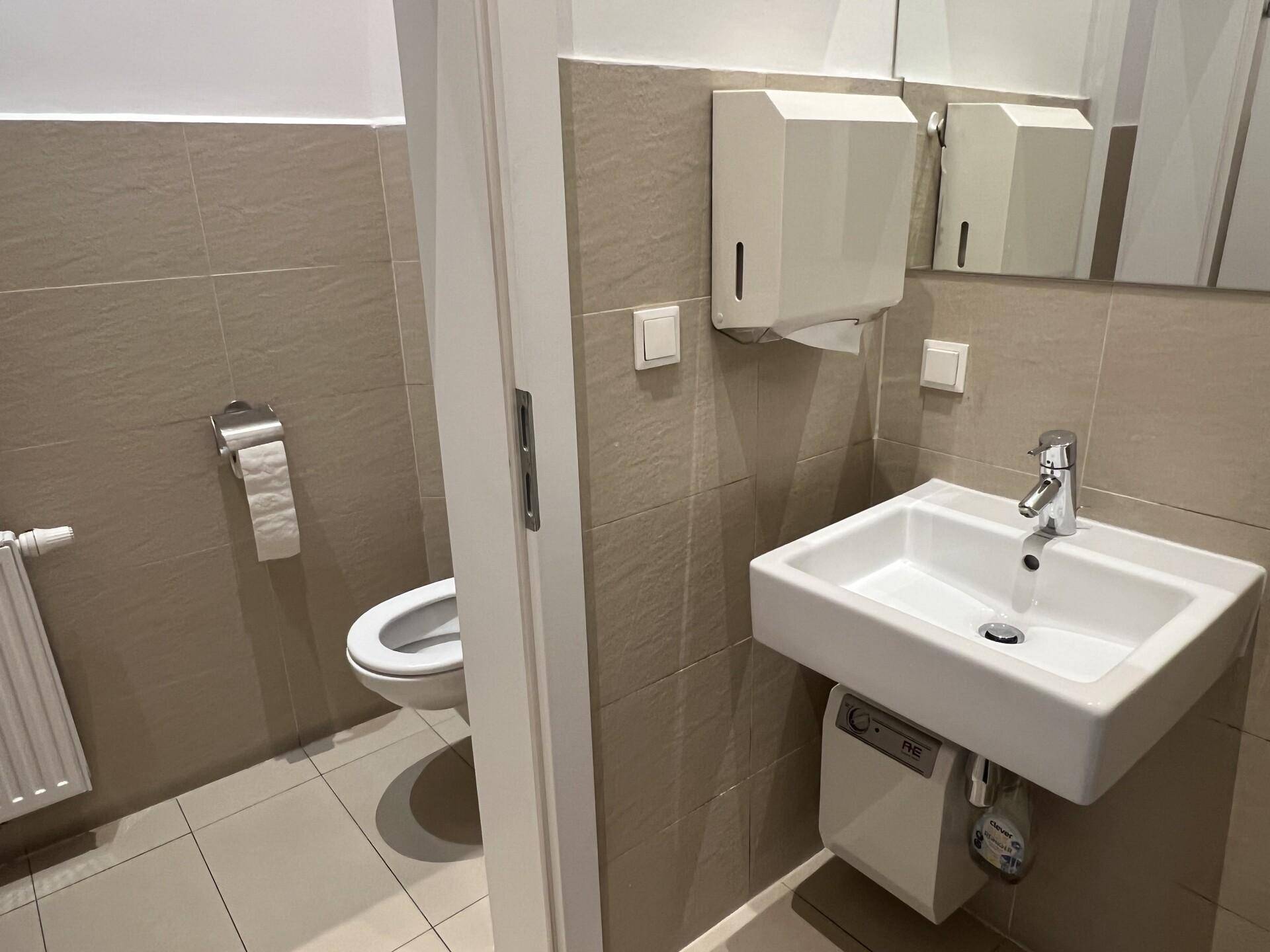 Modernes Gäste-WC mit Waschbecken, Toilette und beigefarbenen Fliesen an Wänden und Boden, in gutem Zustand.