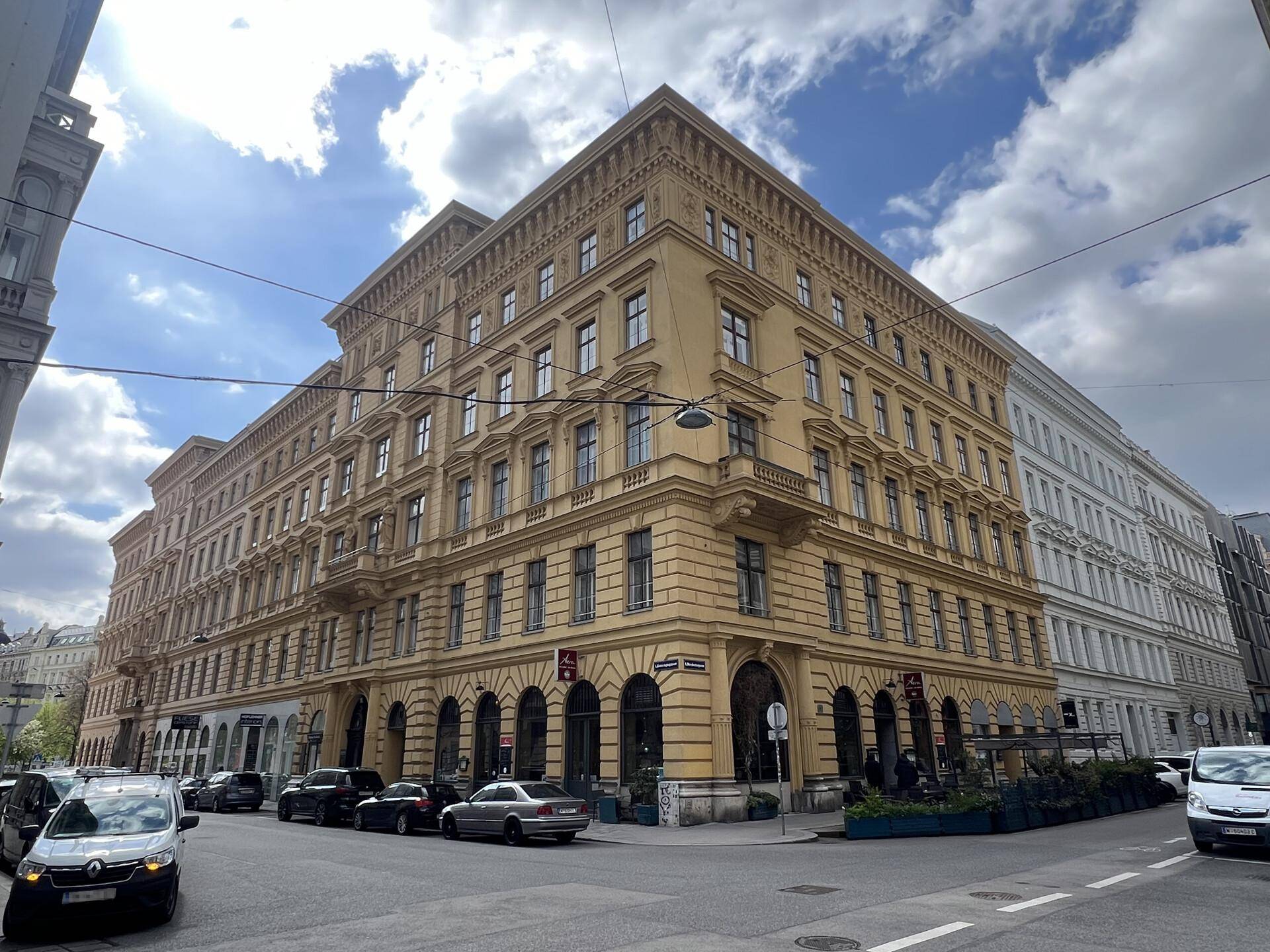 Historisches Eckgebäude mit klassischer Architektur, vielen Fenstern und Geschäften im Erdgeschoss in einer belebten Stadtlage.