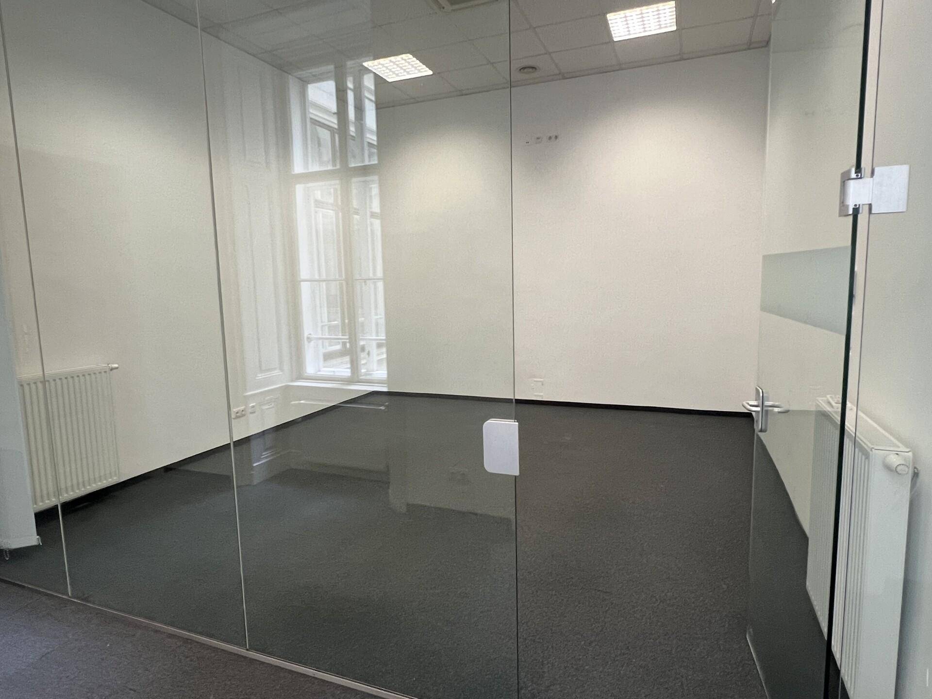 Modernes Büro mit Glaswänden, Teppichboden und großen Fenstern, die viel Tageslicht in den Raum lassen.
