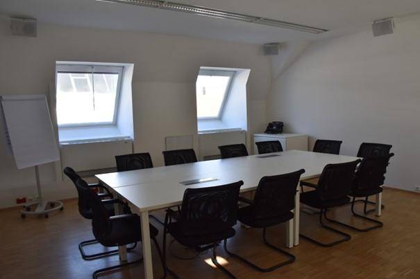 Besprechungsraum im Dachgeschoss mit großem Tisch, vielen Stühlen und schrägen Dachfenstern.