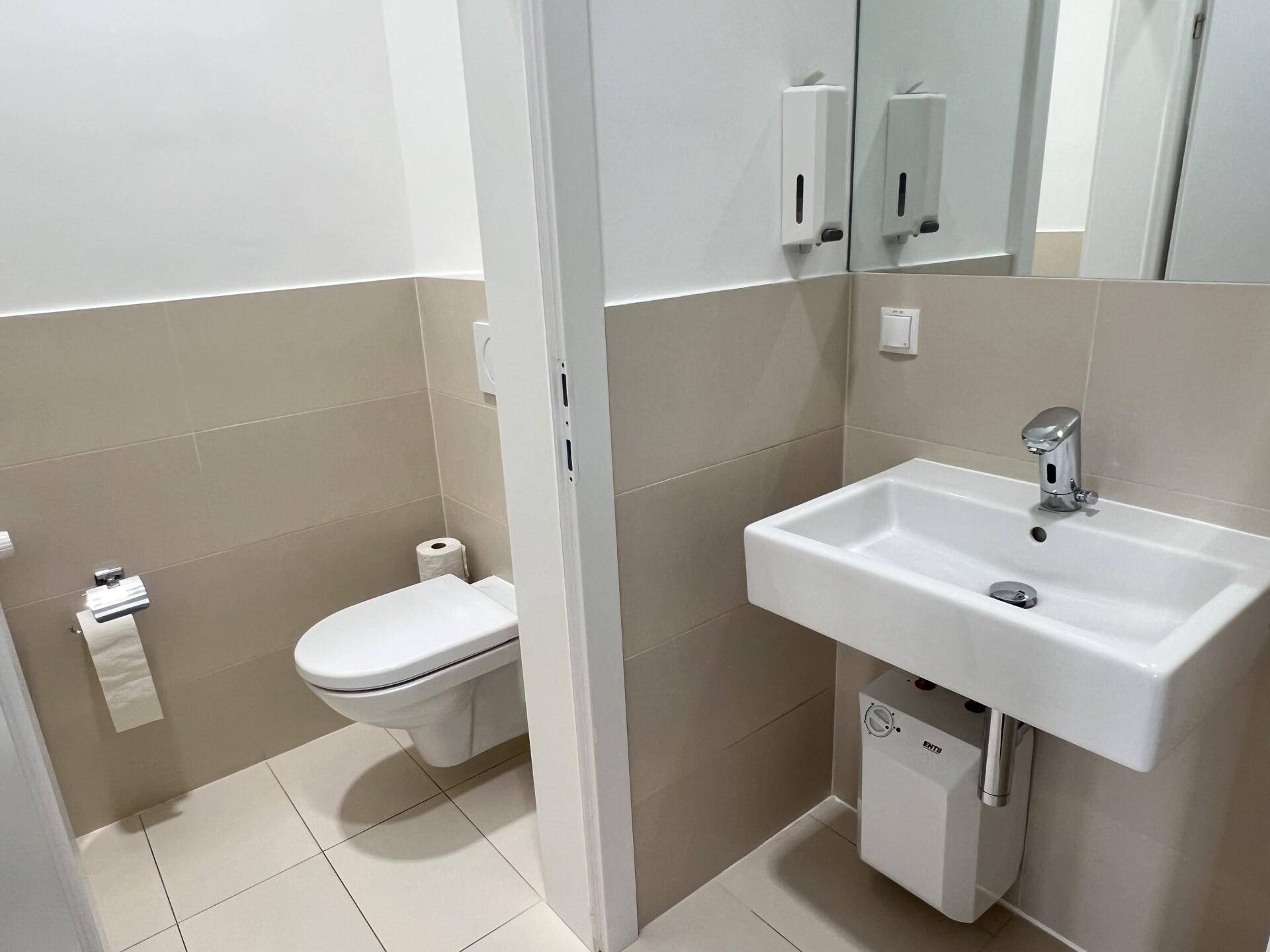 Saubere Toilette mit wandhängendem WC, Waschbecken und beigefarbenen Fliesen an den Wänden.