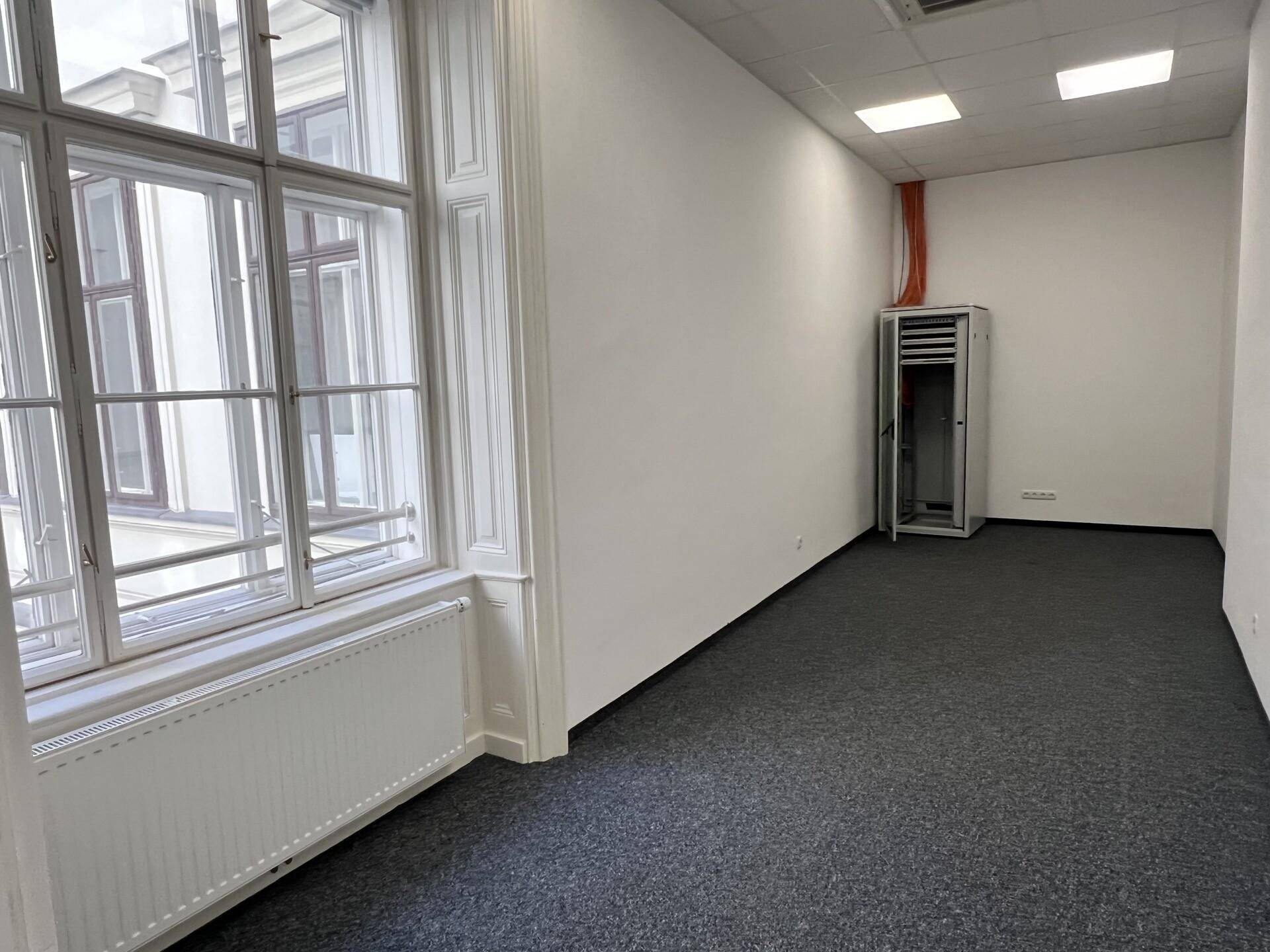 Heller Büroraum mit Teppichboden, großen Fenstern und einem Serverschrank an der Wand.