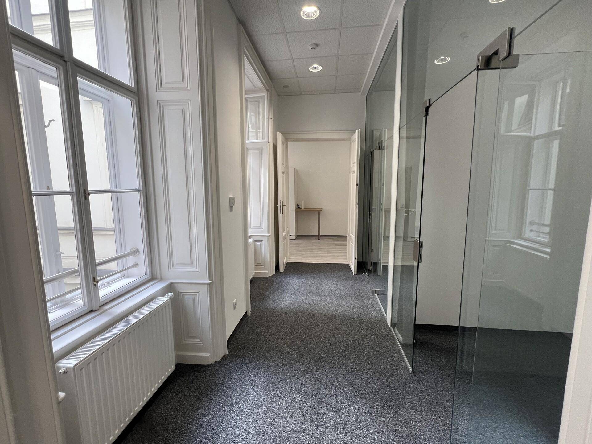 Langer Flur mit Teppichboden, großen Fenstern und modernen Glastrennwänden zu angrenzenden Räumen.