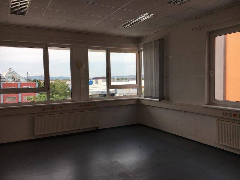 Helles, leeres Büro mit mehreren Fenstern, die einen Blick auf die städtische Umgebung bieten.