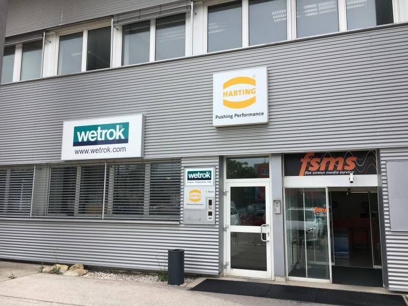 Eingangsbereich eines modernen Geschäftsgebäudes mit Firmenlogos und großen Glastüren.