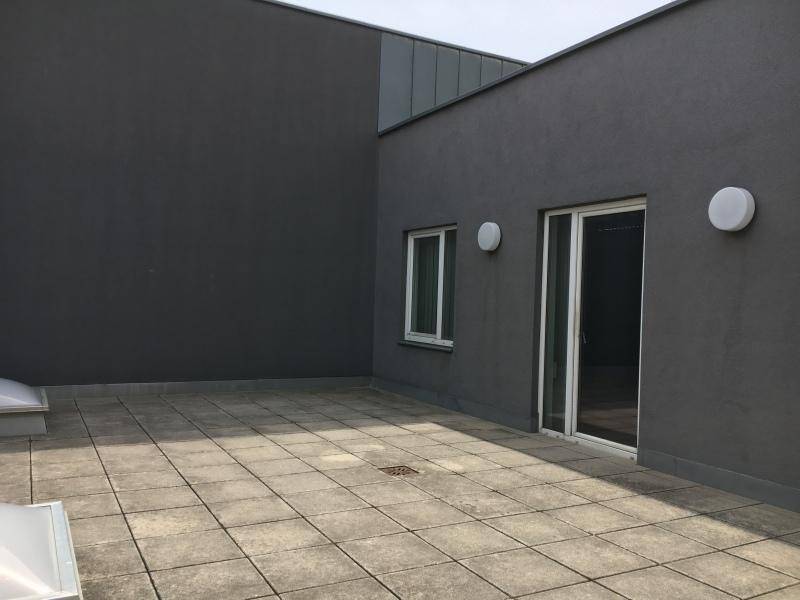 Geräumige Dachterrasse mit grauen Fliesen und einer Glasschiebetür, umgeben von dunklen Wänden.