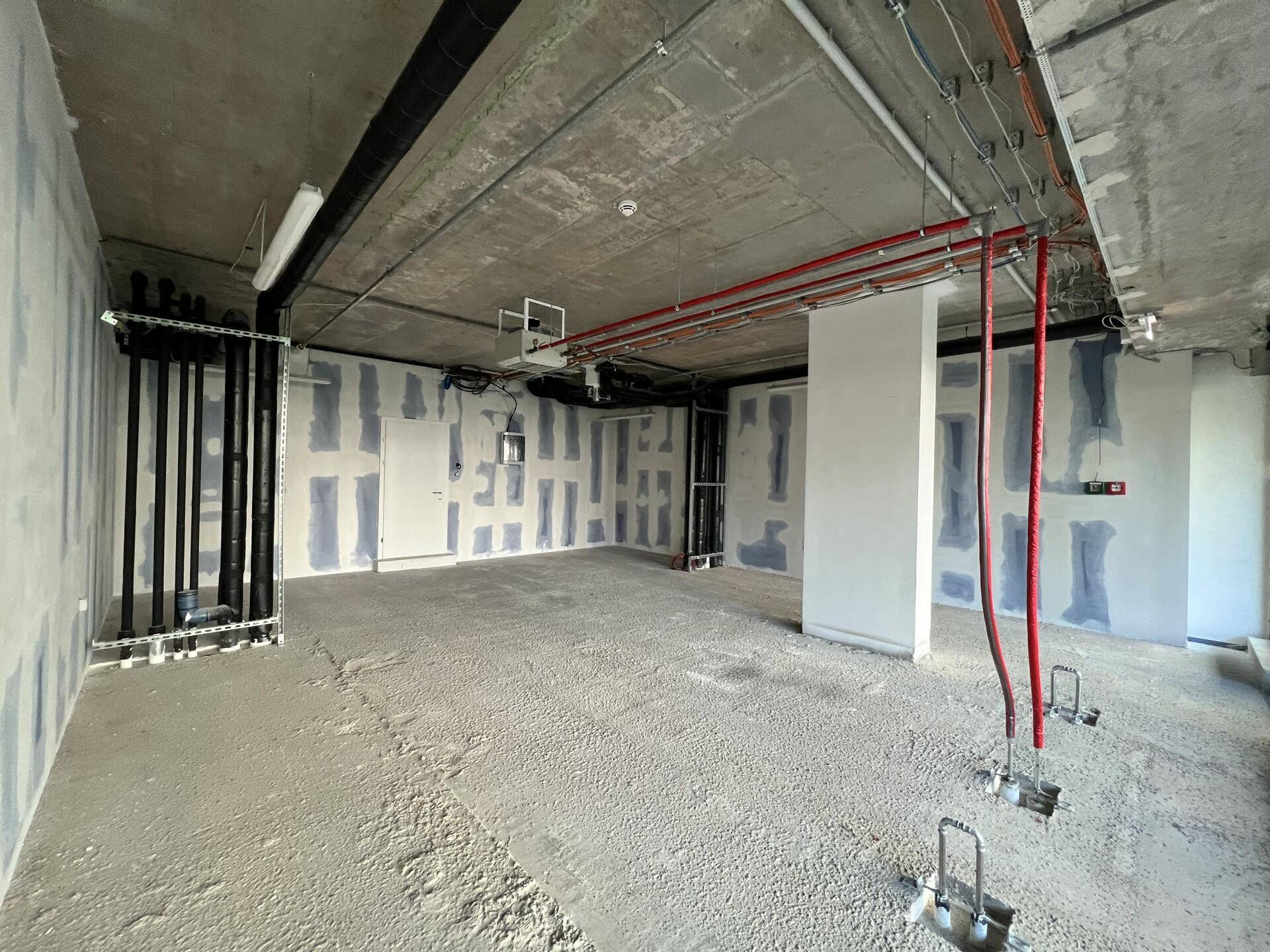 Rohbau-Innenraum mit freiliegenden Installationen, Betonoberflächen und vorbereiteten Wänden für den weiteren Ausbau.