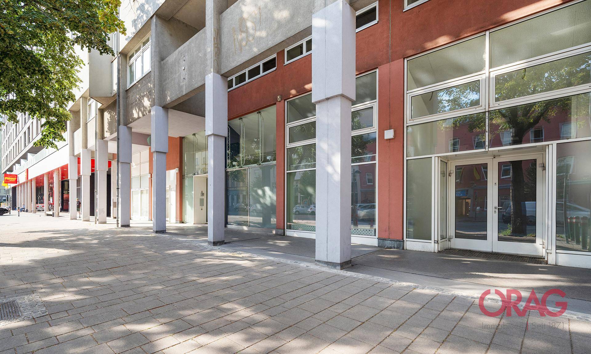 Lange Reihe moderner Geschäftsfassaden mit großen Glasfronten und Säulen entlang einer städtischen Straße.