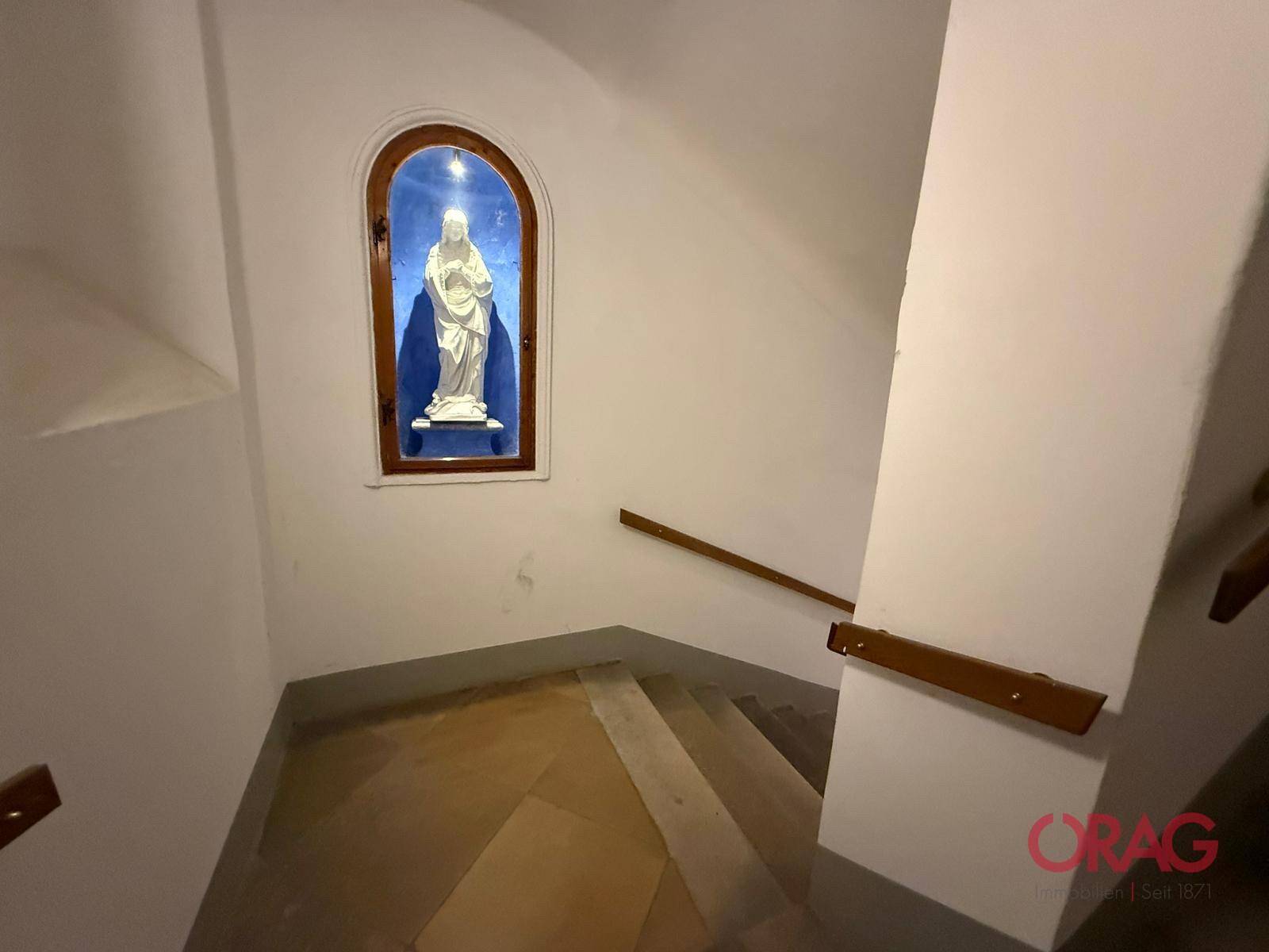 Historisches Treppenhaus mit Steinstufen und einer Nische, die eine religiöse Statue beherbergt.
