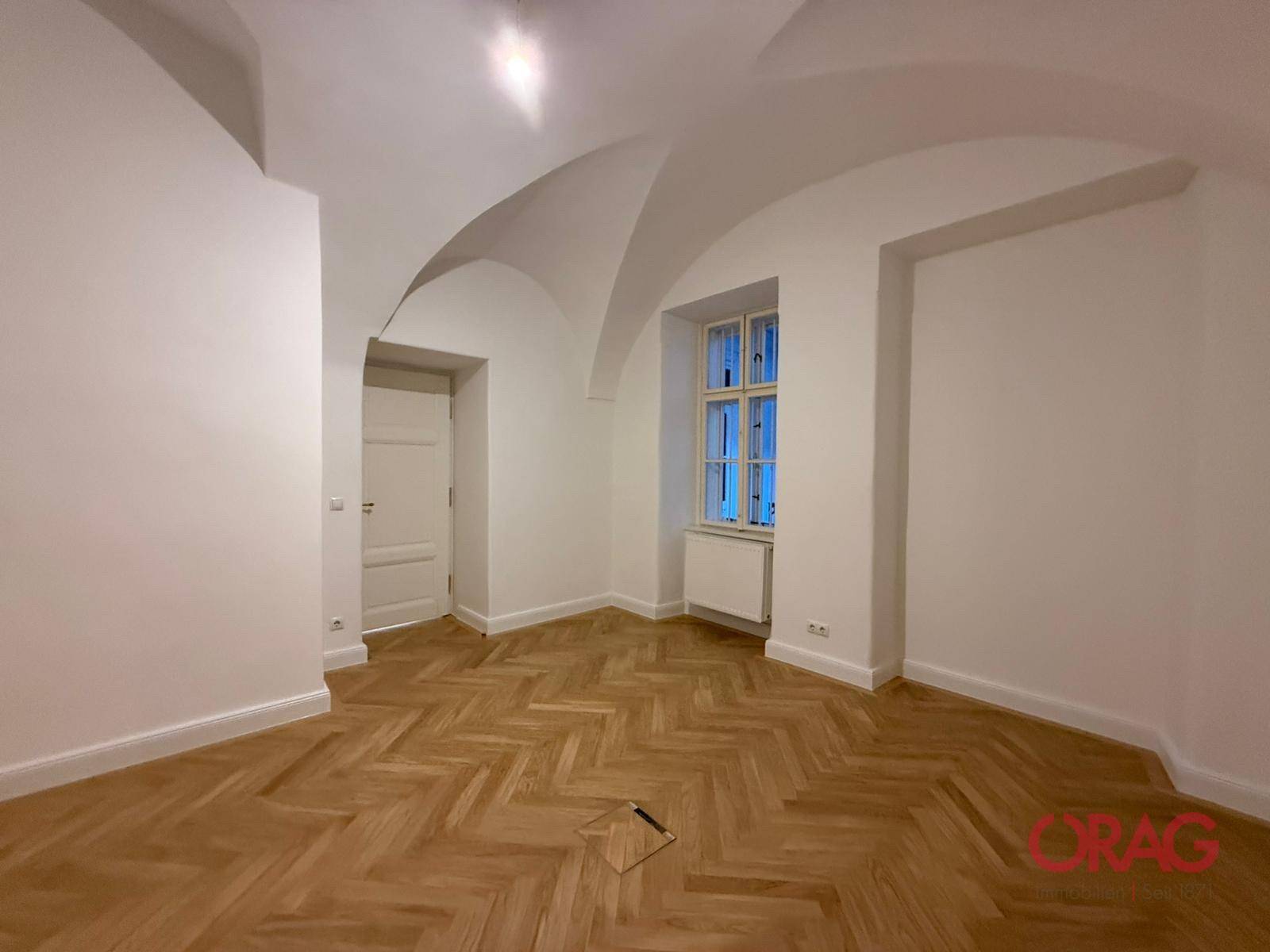 Helles Zimmer mit elegantem Fischgrätparkett und einer beeindruckenden Gewölbedecke, die historischen Charme verleiht.