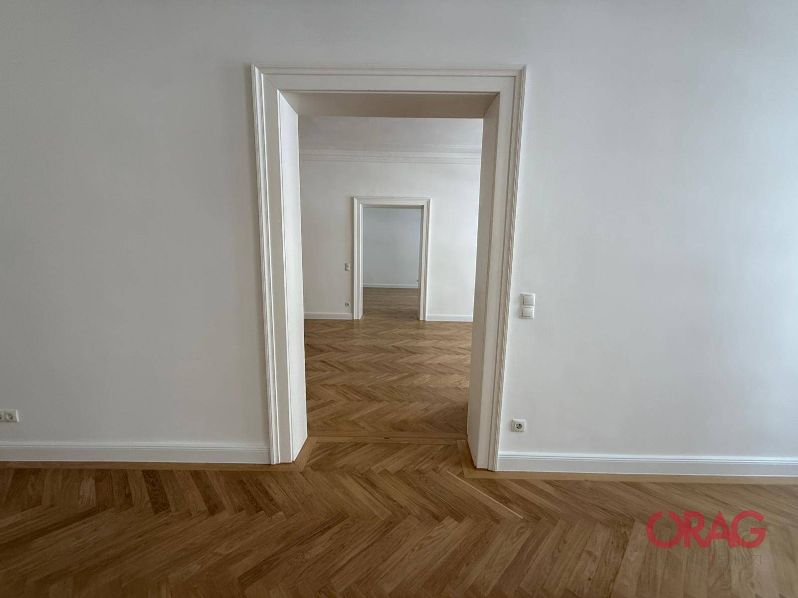 Blick durch eine Reihe offener Türen, die die Weitläufigkeit der Räume mit Fischgrätparkett hervorheben.