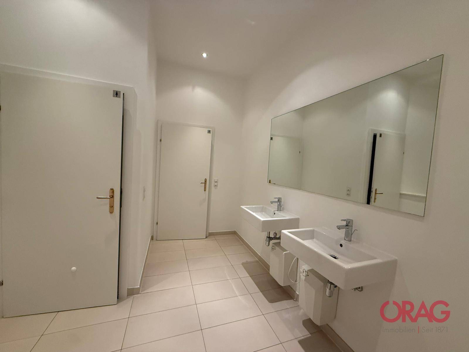 Helles Badezimmer mit zwei modernen Waschbecken, einem großen Spiegel und hellen Fliesen.