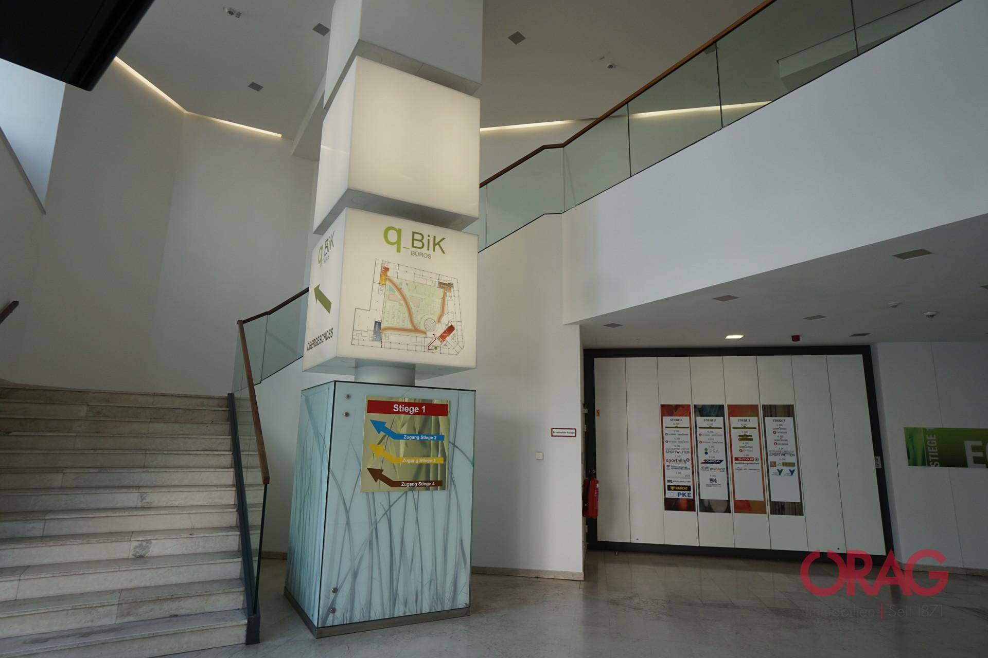 Moderner Eingangsbereich mit Treppe und einer beleuchteten Informationssäule.