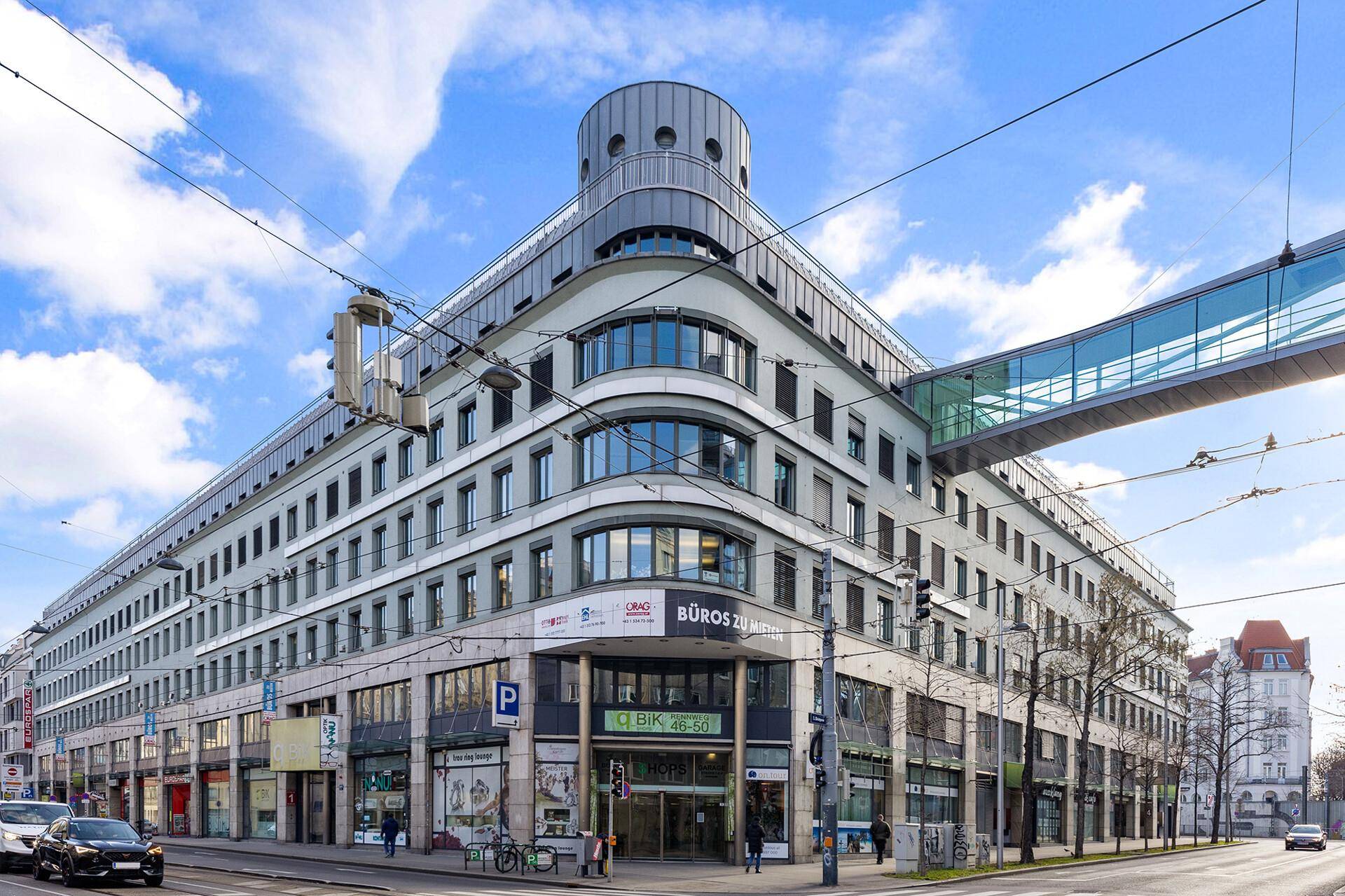 Großes, modernes Bürogebäude an einer belebten Straße mit markanter Architektur und Glasbrücke.