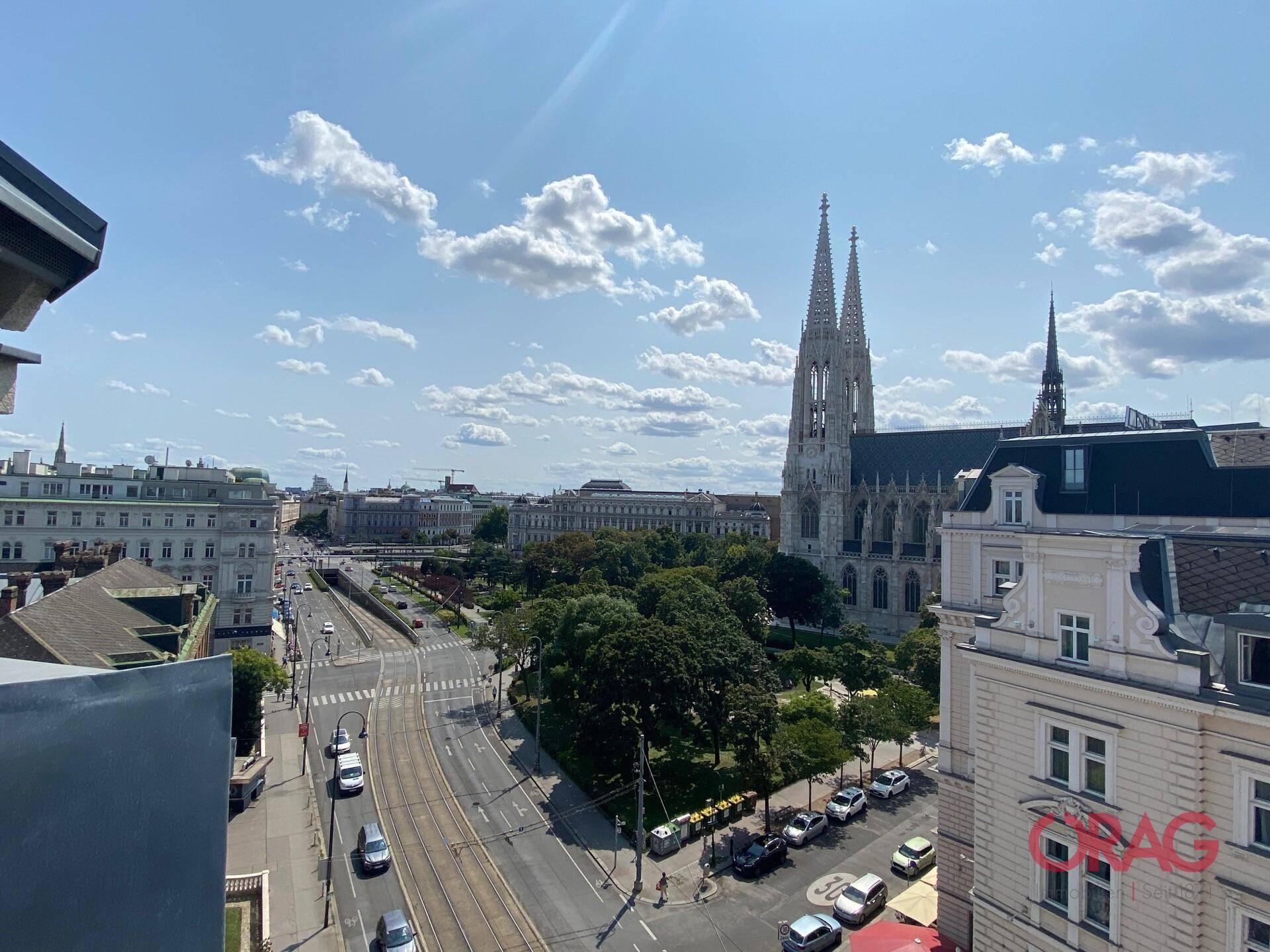 Panoramablick über die Stadt mit historischer Kirche und belebten Straßen unter blauem Himmel.