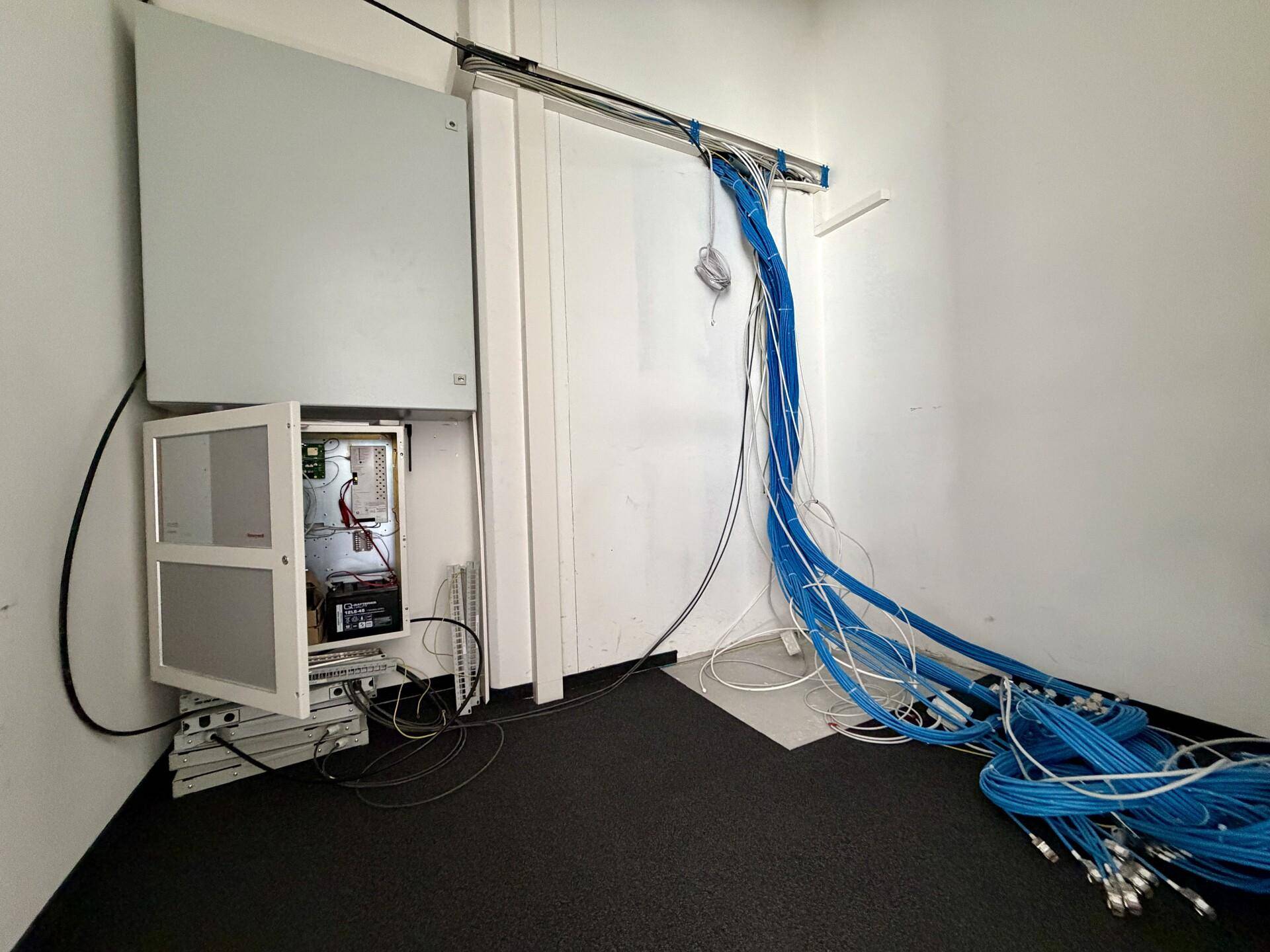 Technikraum mit Serverracks und umfangreicher Verkabelung, der die Infrastruktur des Gebäudes beherbergt.