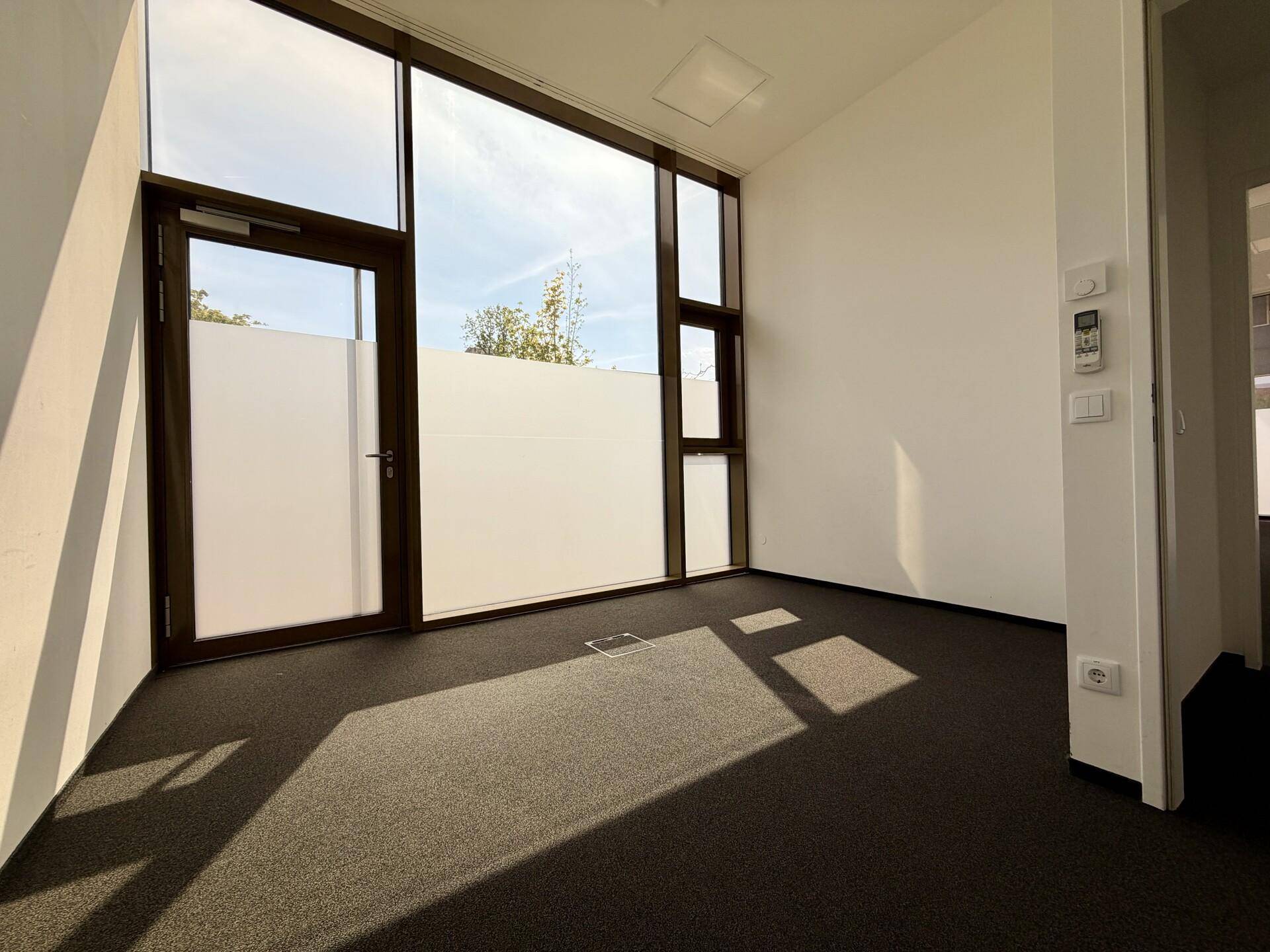 Heller Bürobereich mit Teppichboden und raumhohen Fenstern, die eine angenehme Arbeitsatmosphäre schaffen.