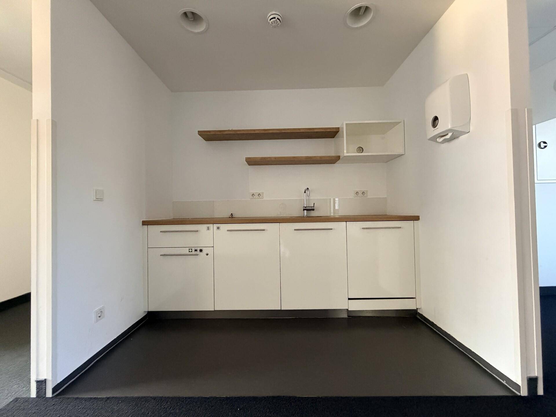 Kleine, moderne Teeküche mit weißen Schränken, Holztheke und integriertem Geschirrspüler.