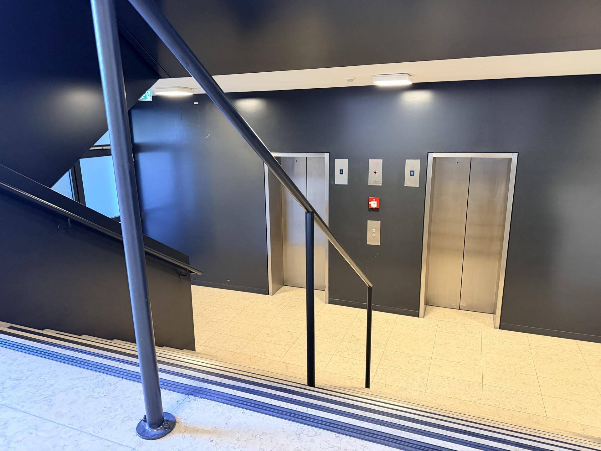 Moderner Eingangsbereich mit Treppe und zwei Aufzügen, die zu den oberen Etagen führen.