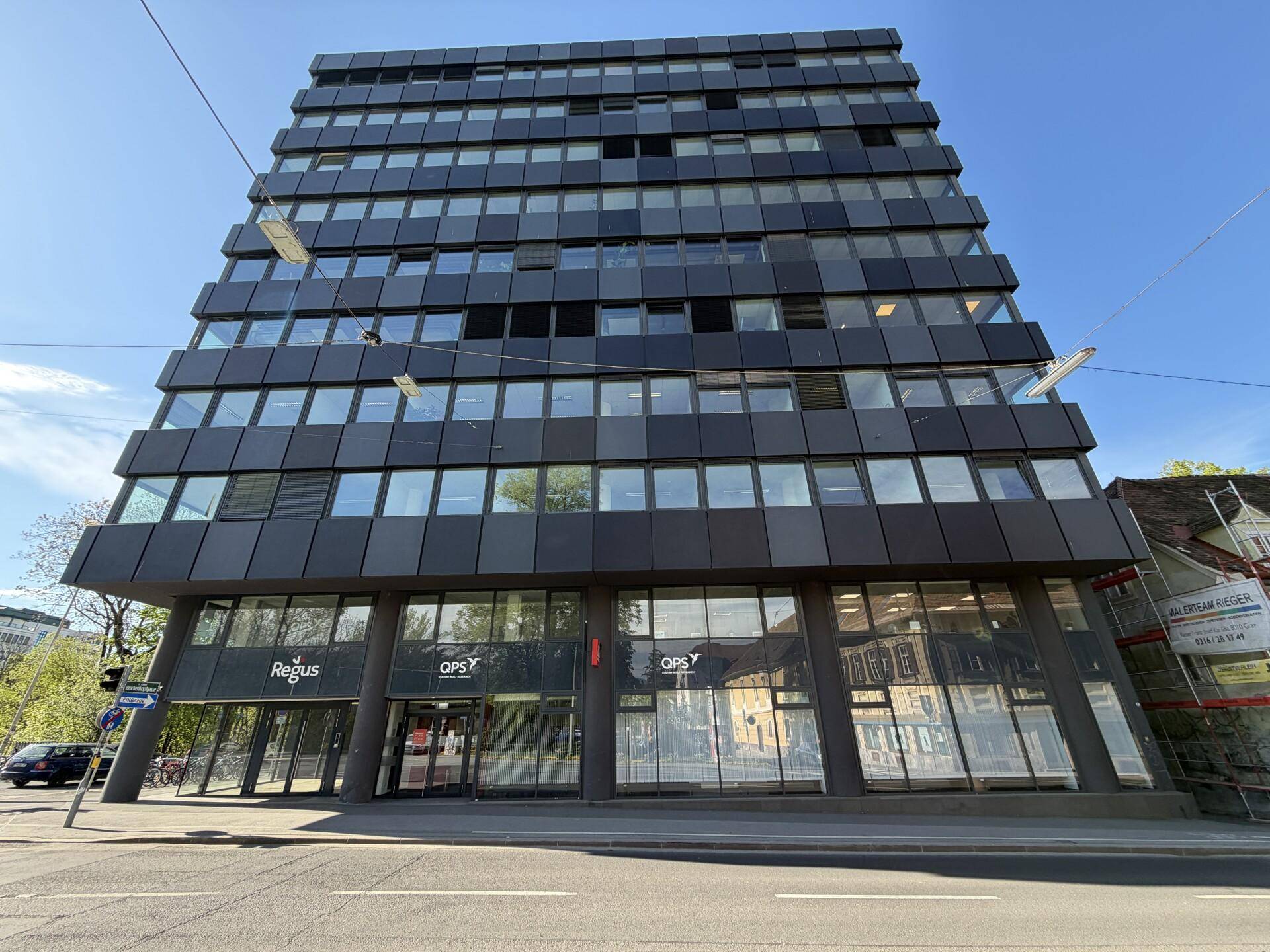 Großes, modernes Bürogebäude mit dunkler Fassade und vielen Fenstern an einer belebten Straße in der Stadt.