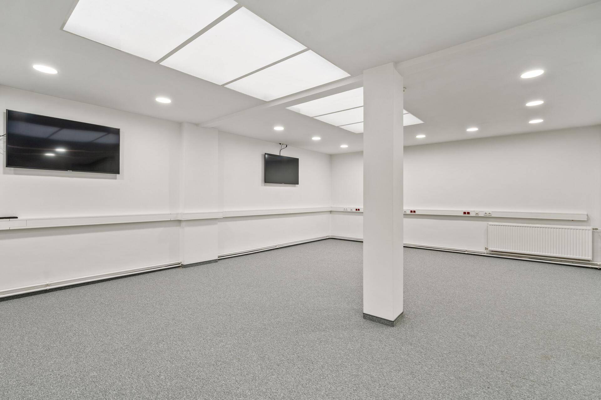 Moderner Konferenzraum mit Teppichboden, integrierten Bildschirmen und Deckenbeleuchtung für Präsentationen.