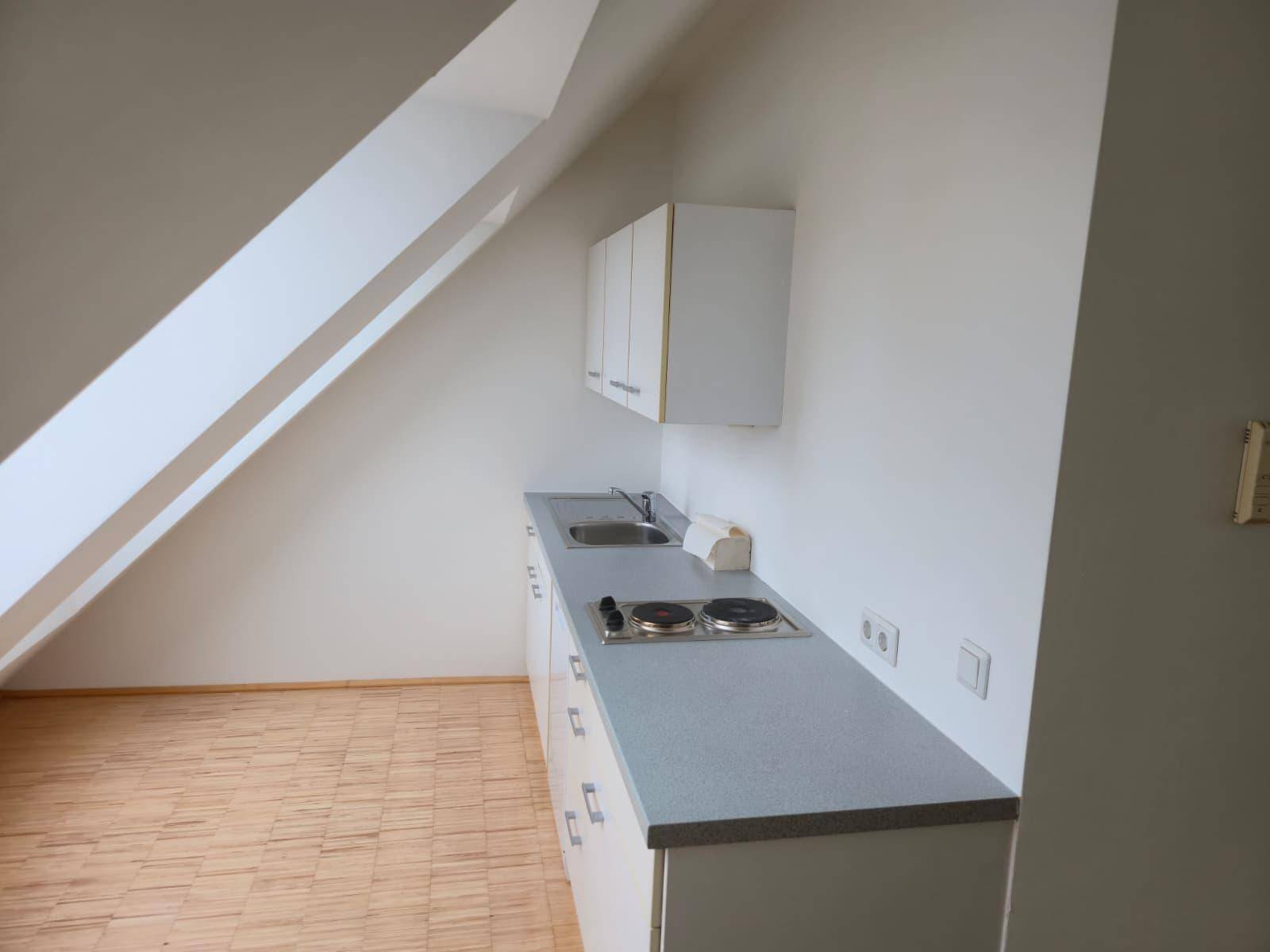 Kleine Küchenzeile im Dachgeschoss mit Spüle, Kochplatten und Oberschränken.