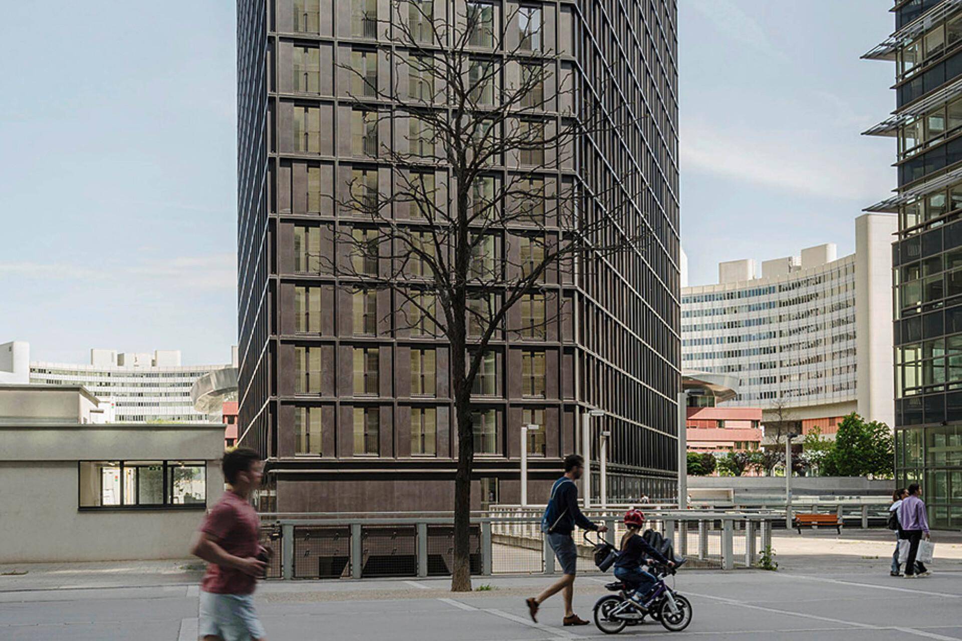 Das moderne Hochhaus in seiner städtischen Umgebung mit Passanten und umliegenden Gebäuden.