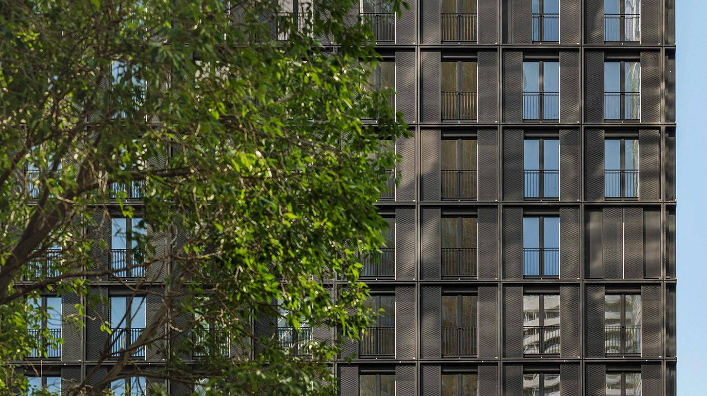 Detail der Gebäudefassade mit grünen Bäumen im Vordergrund, die eine natürliche Umgebung schaffen.