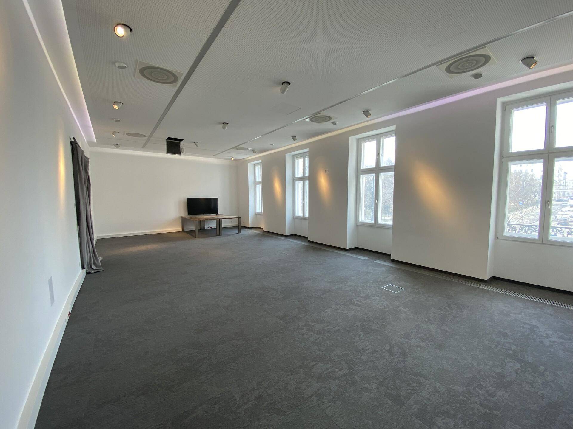 Großer, leerer Raum mit Teppichboden, vielen Fenstern und moderner Deckenbeleuchtung, ideal für Büros.