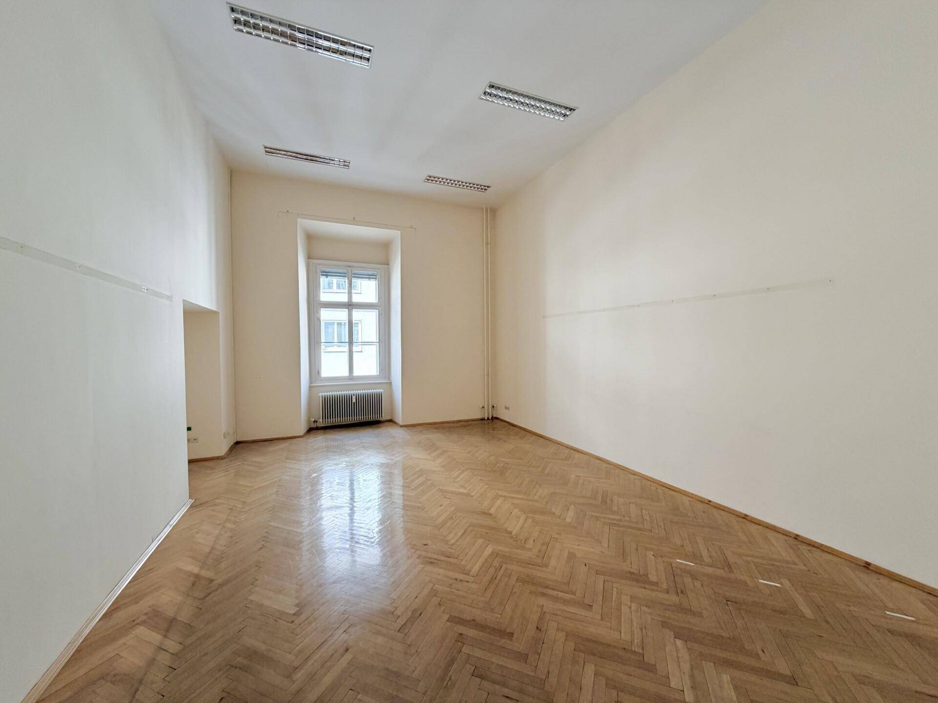 Geräumiges Büro mit Fischgrätparkett, hohen Decken und einem Fenster.