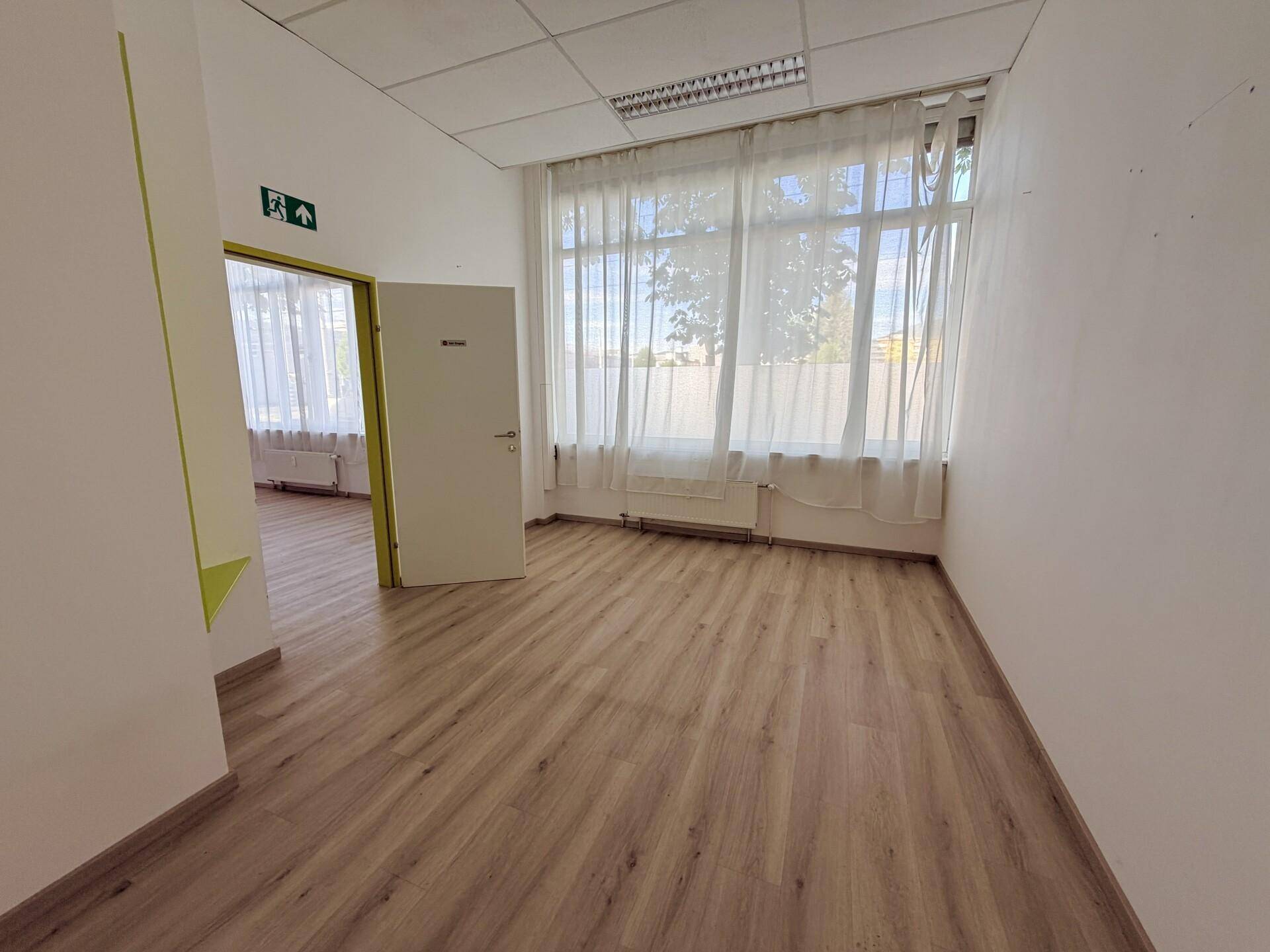 Heller Büroraum mit Laminatboden, großen Fenstern und Vorhängen, die für Privatsphäre sorgen.