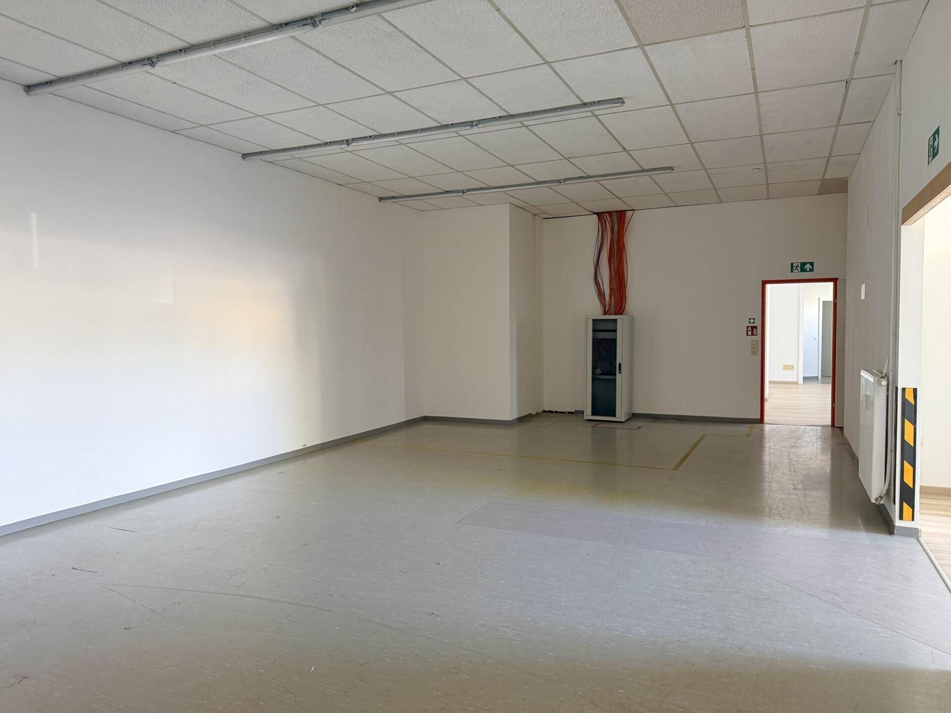 Großer, leerer Raum mit Vinylboden und abgehängter Decke, bereit für individuelle Gestaltung und Nutzung.