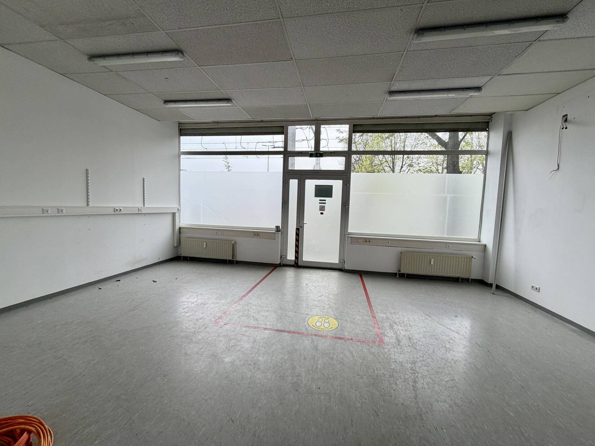 Geräumiger, heller Raum mit großen Fenstern und einer Eingangstür, ideal für Einzelhandel oder Büroflächen.