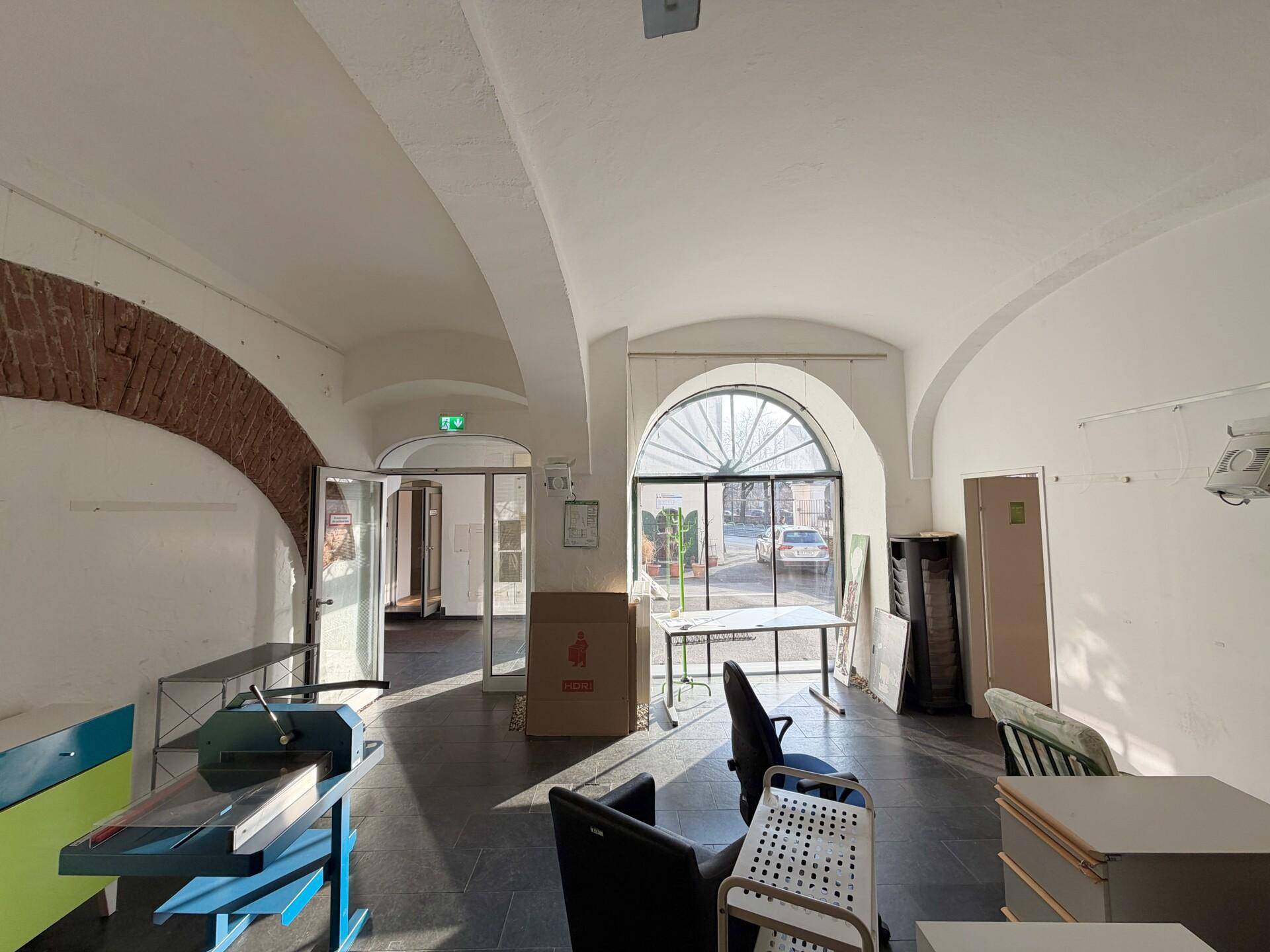 Geräumiger Bürobereich mit gewölbter Decke, großen Fenstern und dunklem Fliesenboden.