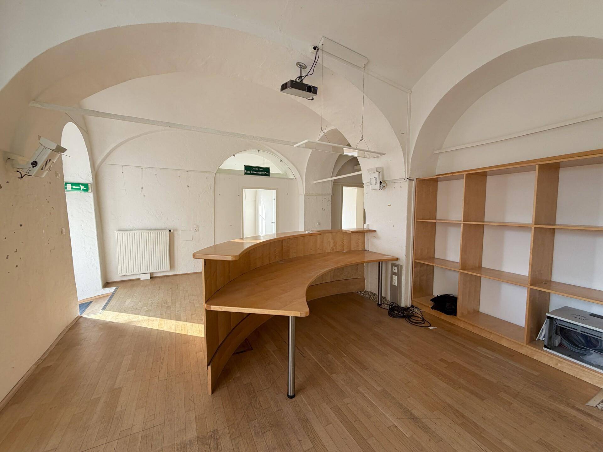 Geräumiger Bürobereich mit gewölbter Decke, Holztheke und Regalen an der Wand.