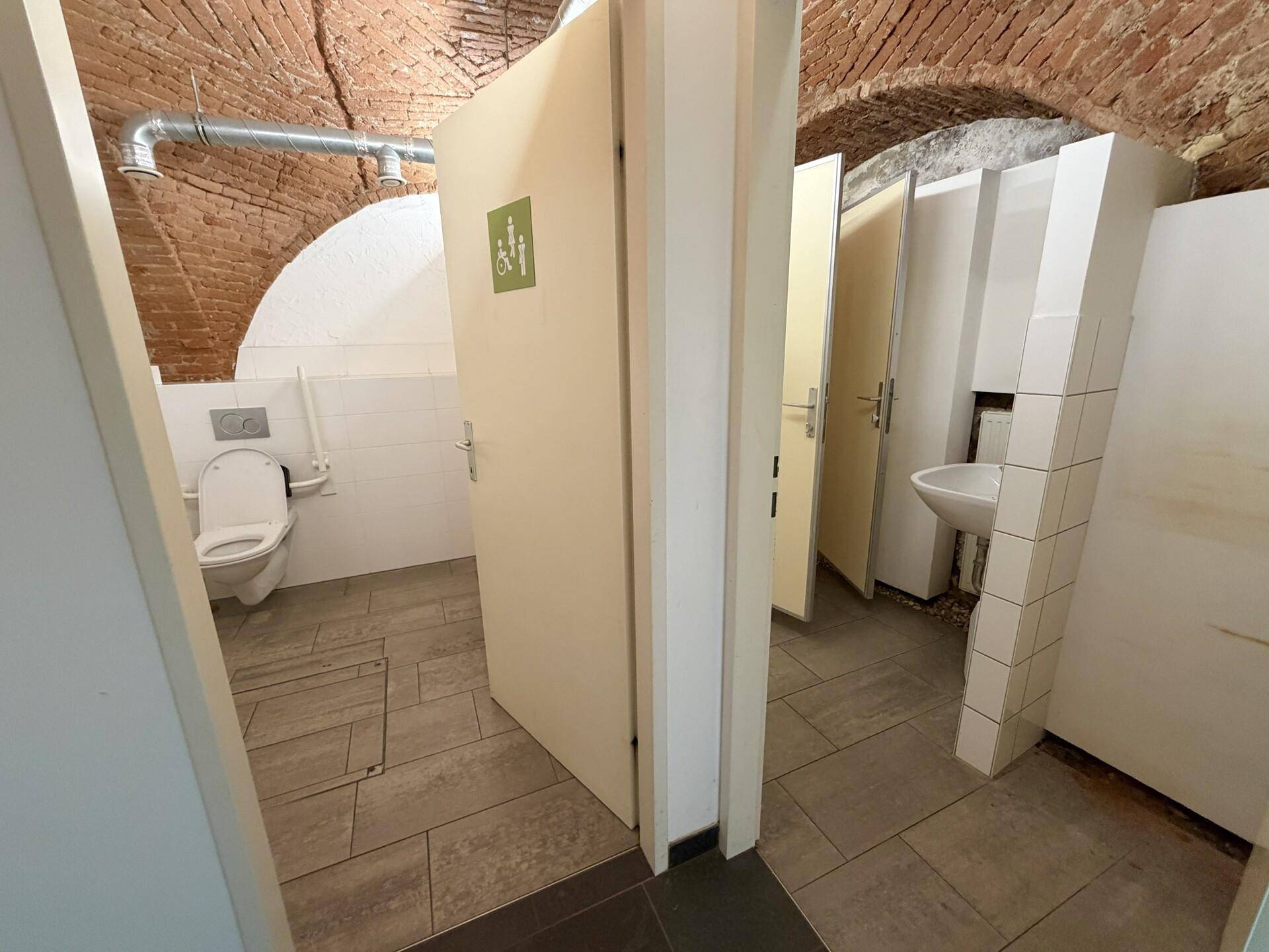 Mehrere Toilettenkabinen in einem Raum mit gewölbter Ziegeldecke und Fliesenboden.