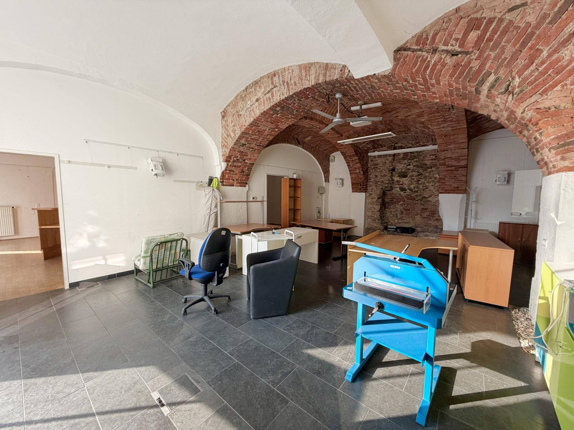 Großes Büro mit freiliegenden Ziegelgewölben, dunklen Fliesen und verschiedenen Büromöbeln.